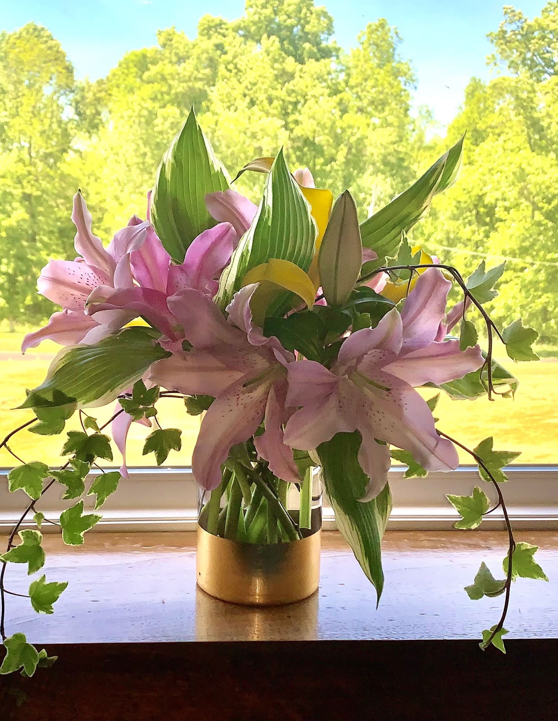 Pink lilies arranged in a gold vase with trailing ivy