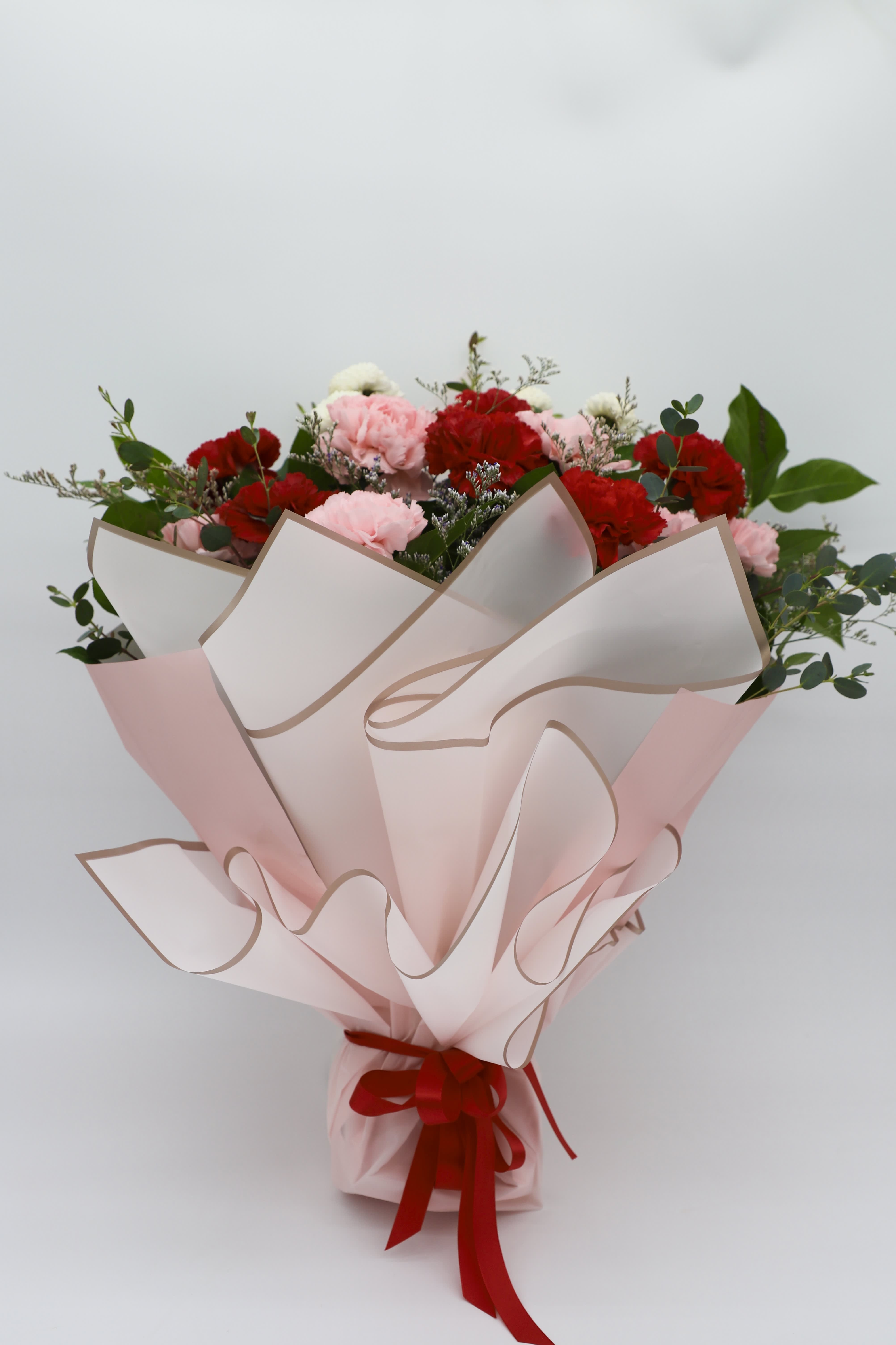Pink and red carnation bouquet wrapped in pale pink paper with a red ribbon