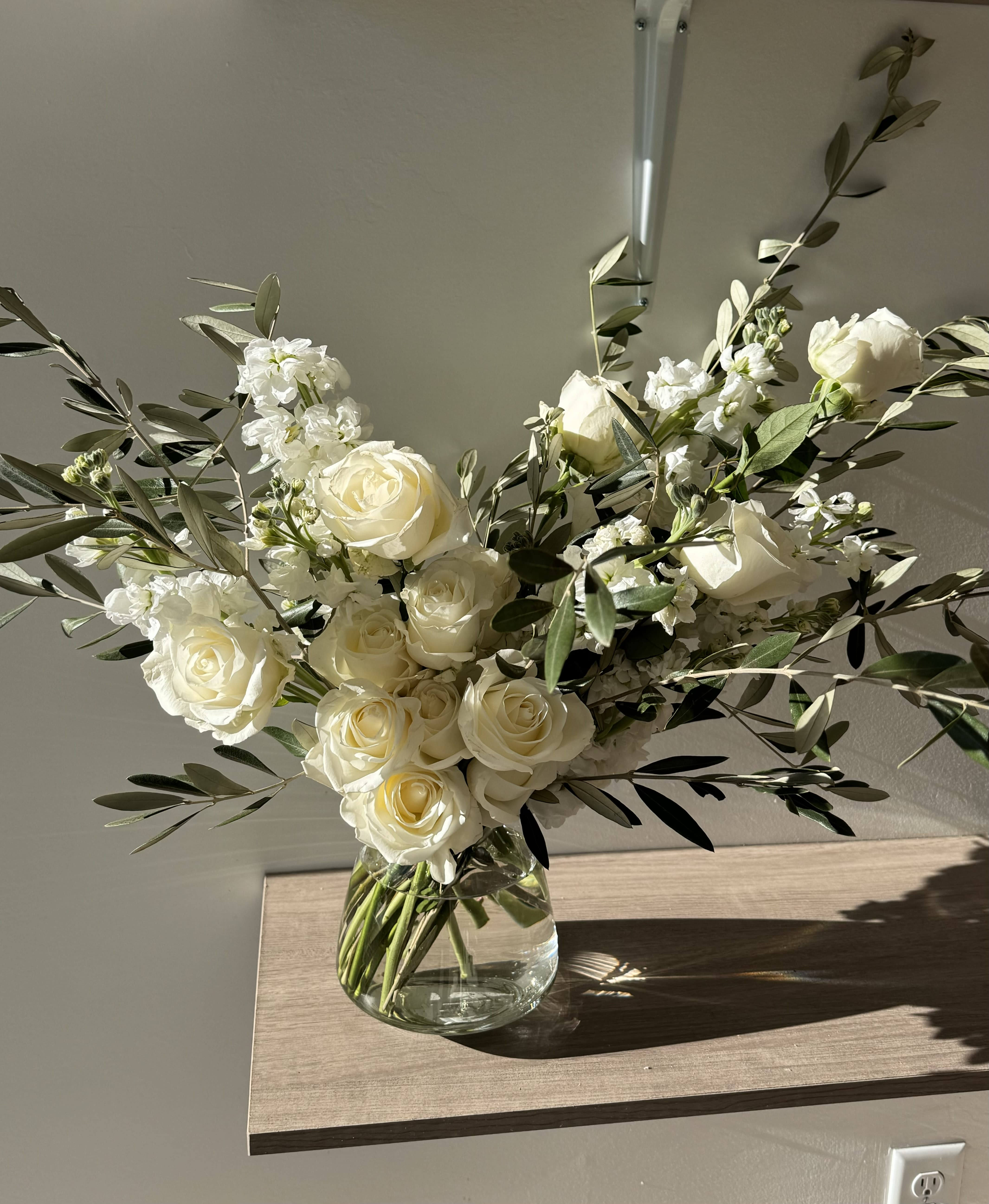 White roses and small white flowers in a clear glass vase