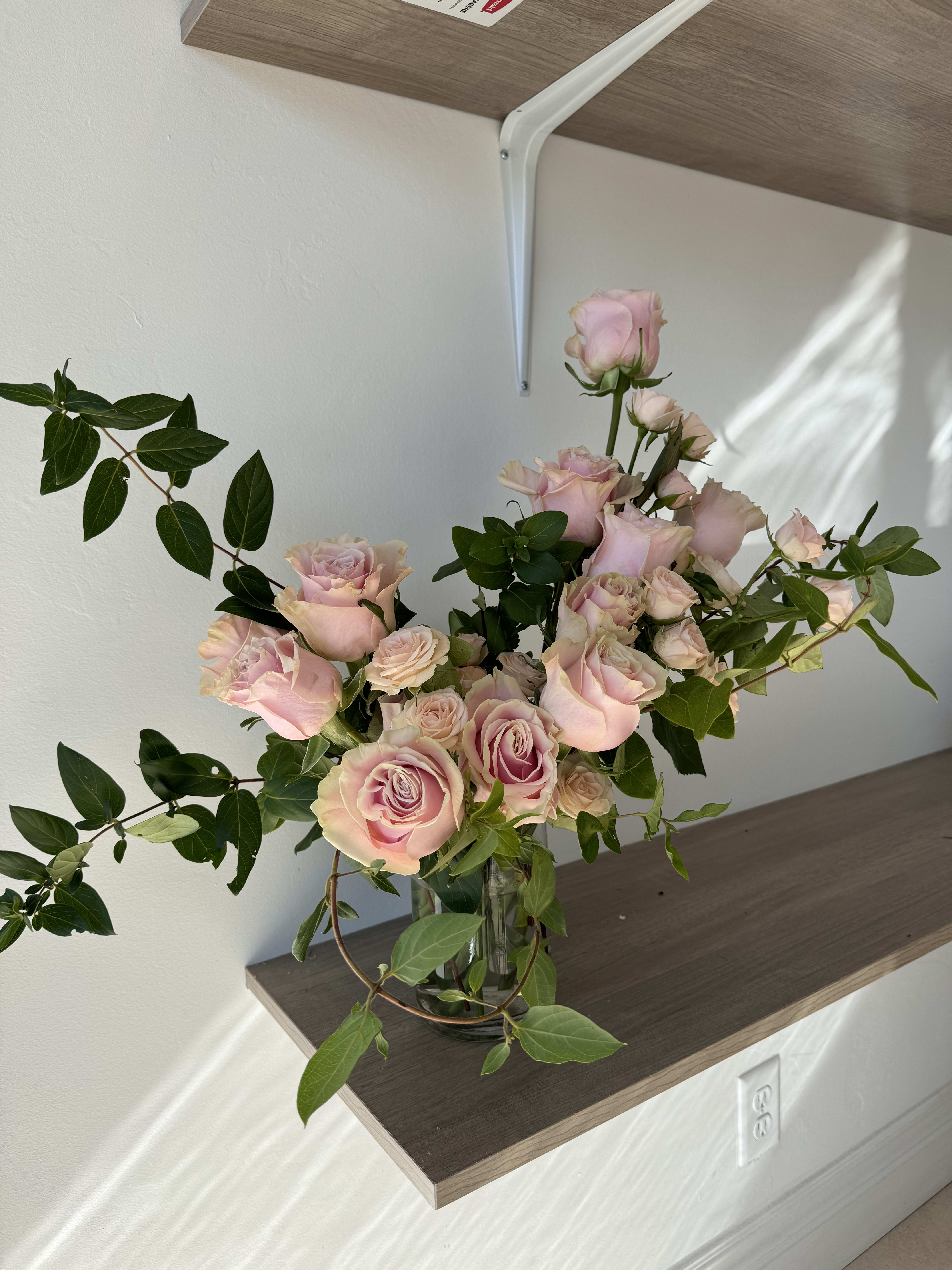 Pink roses arranged in a clear glass vase with trailing greenery