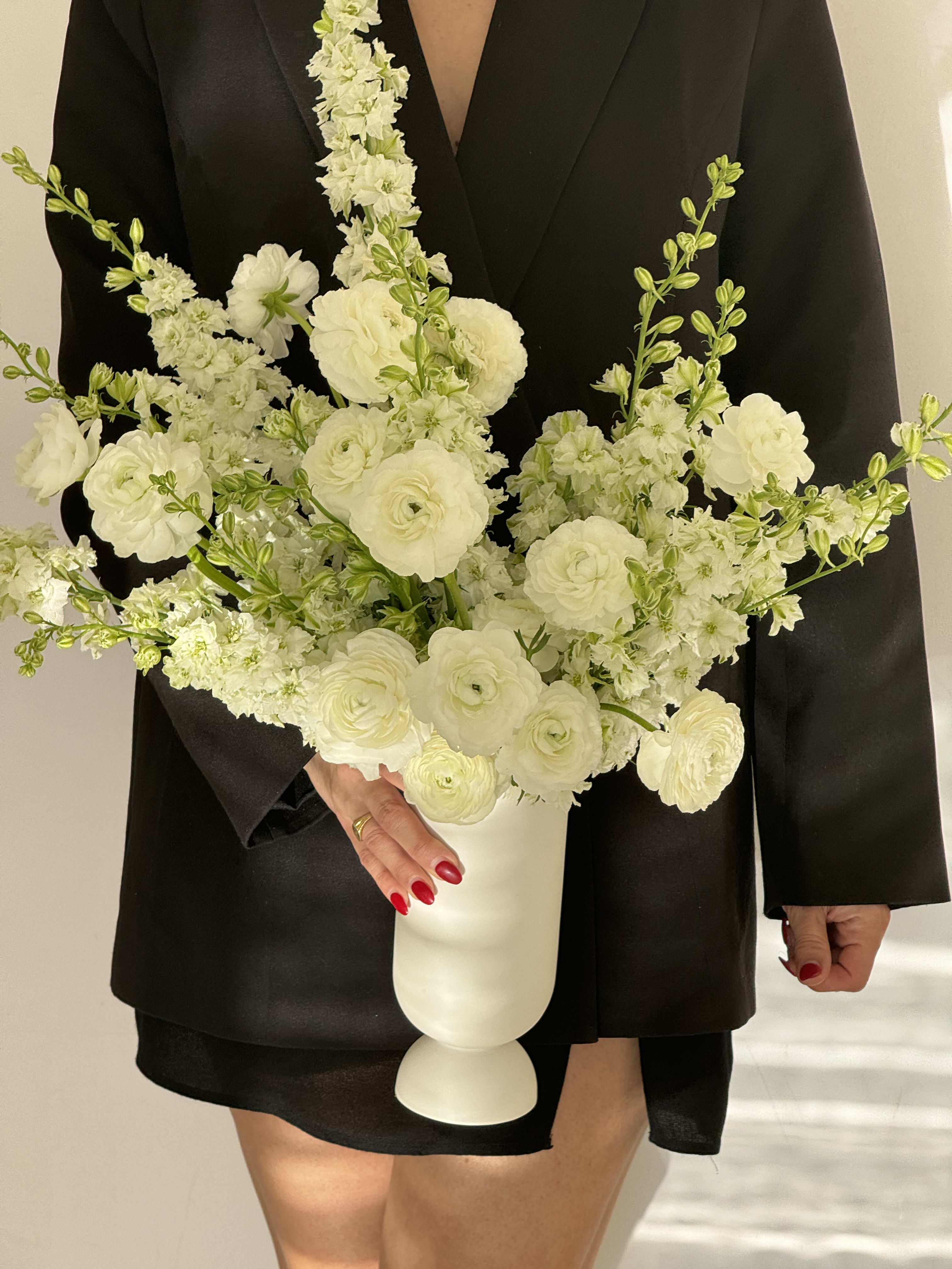 White floral arrangement in a white pedestal vase held against a black outfit