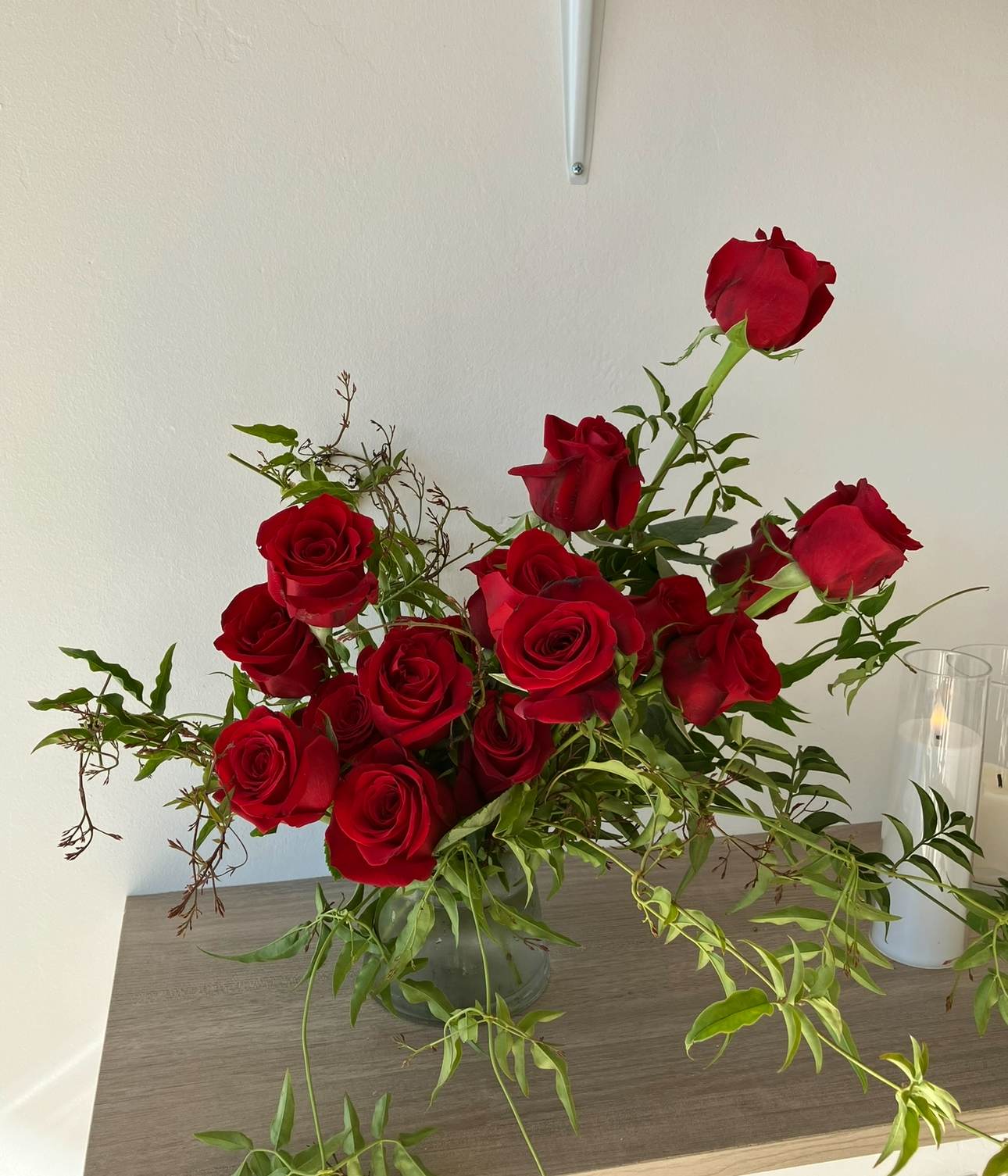 Red roses arranged in a clear glass vase with trailing greenery