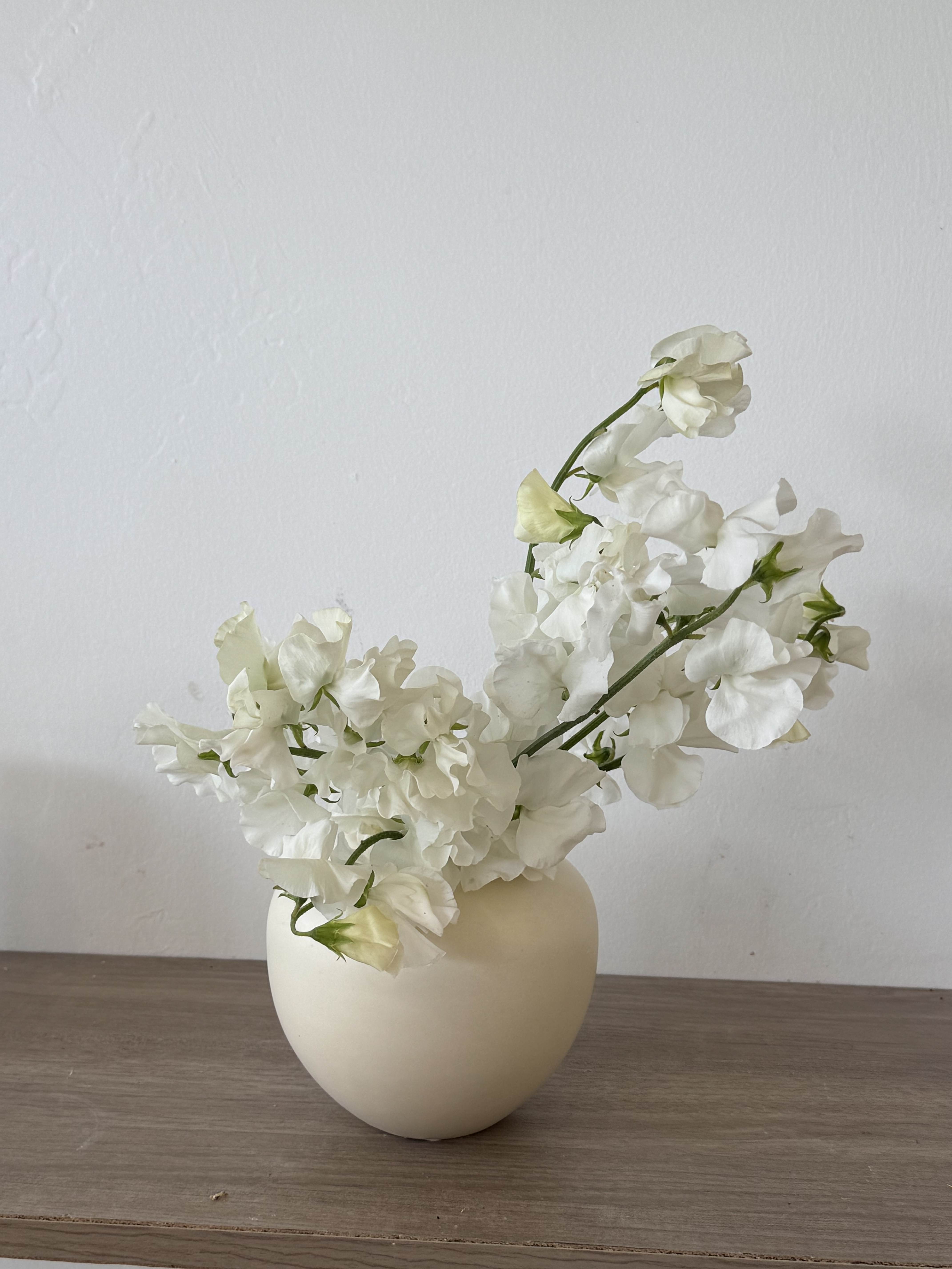 White sweet pea flowers in a cream vase on a wooden surface