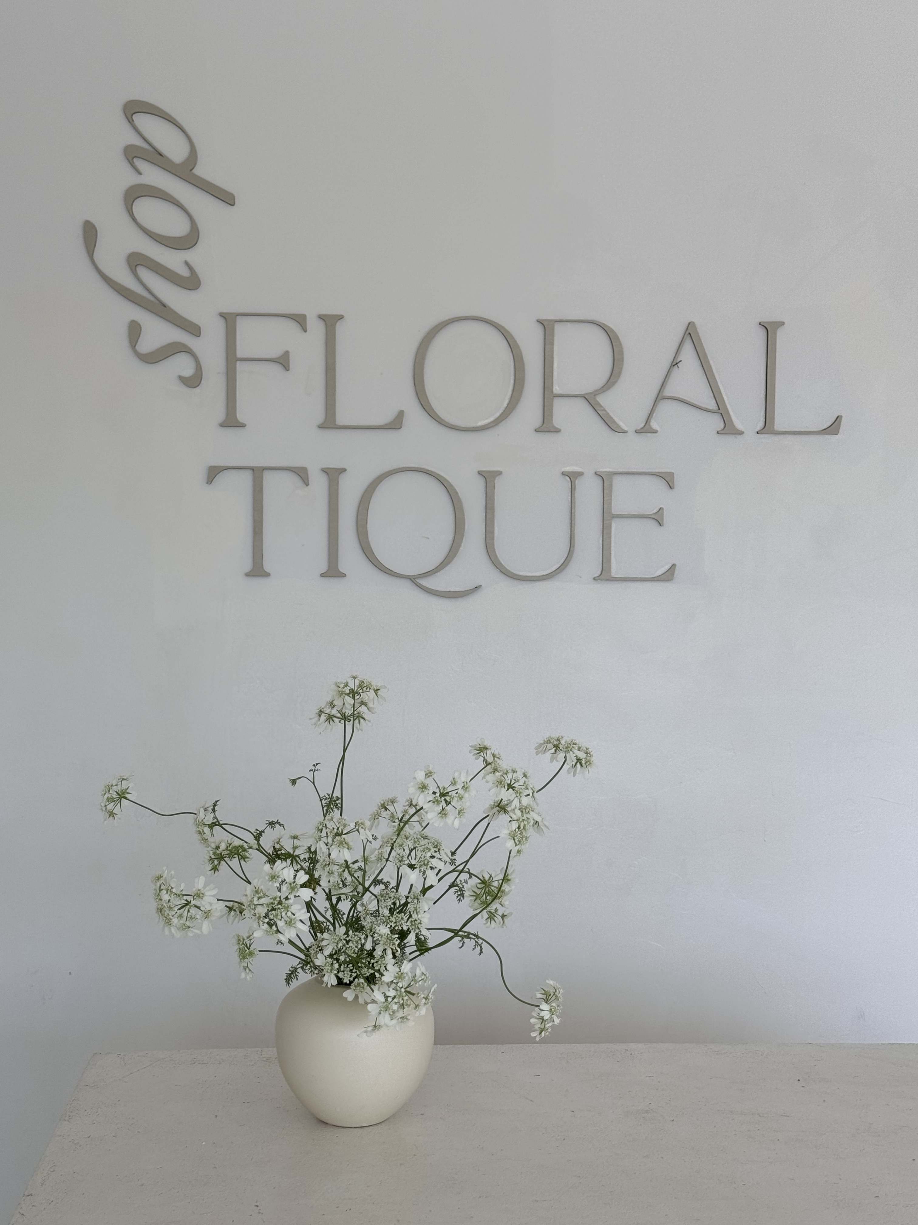 White wildflower arrangement in a cream vase beneath wall lettering