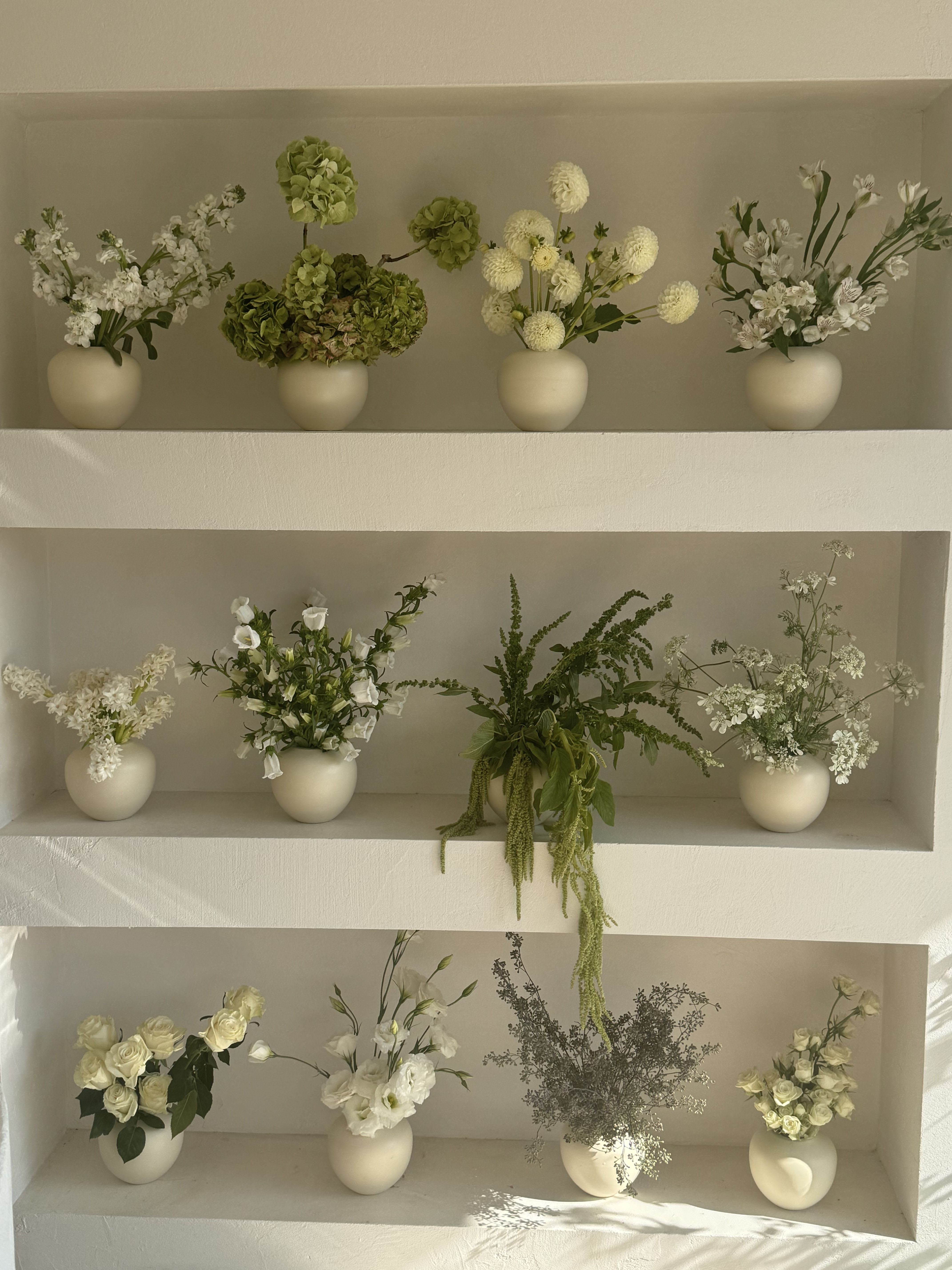 Shelved display of small white floral arrangements in cream vases