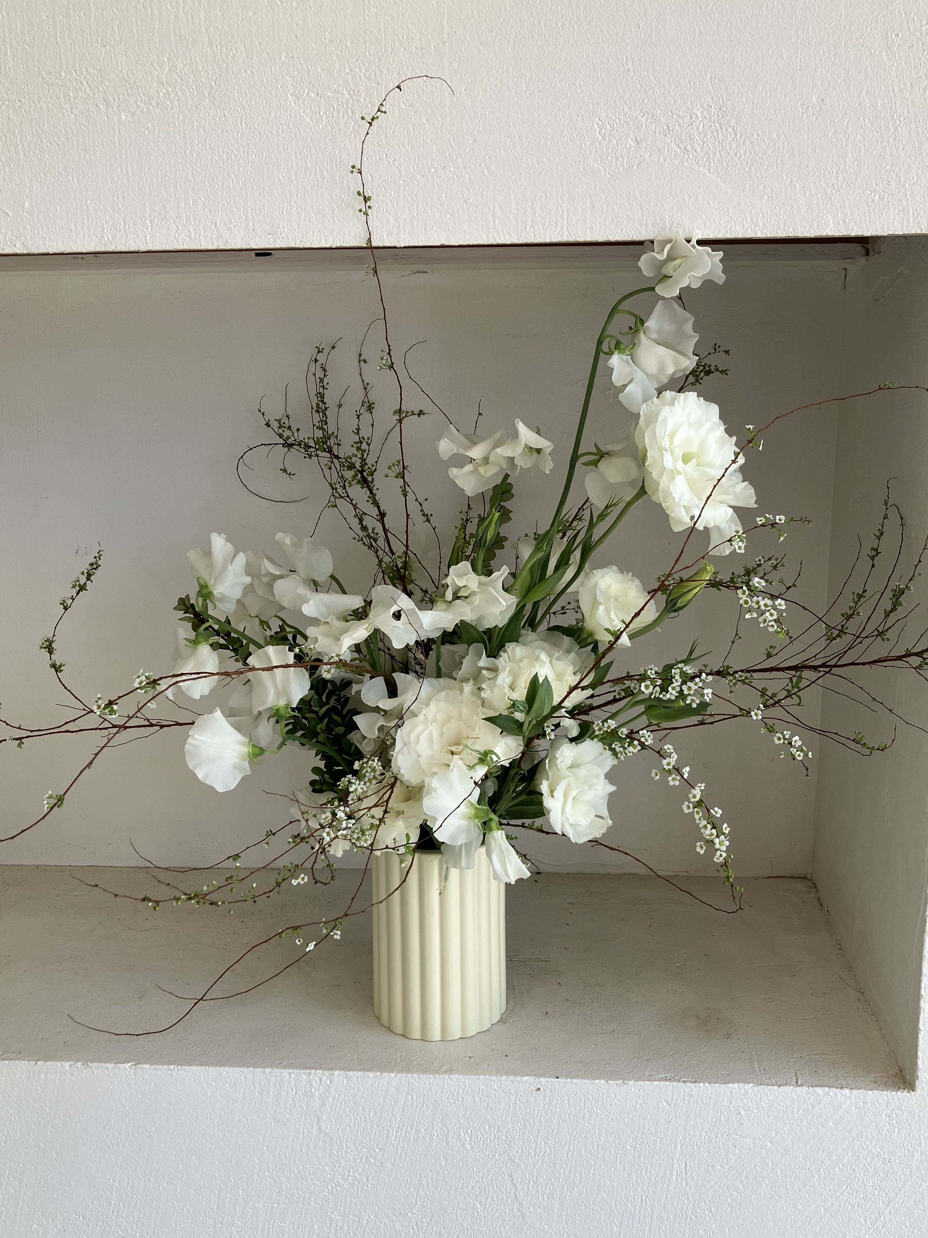 White floral arrangement in a ribbed cream vase