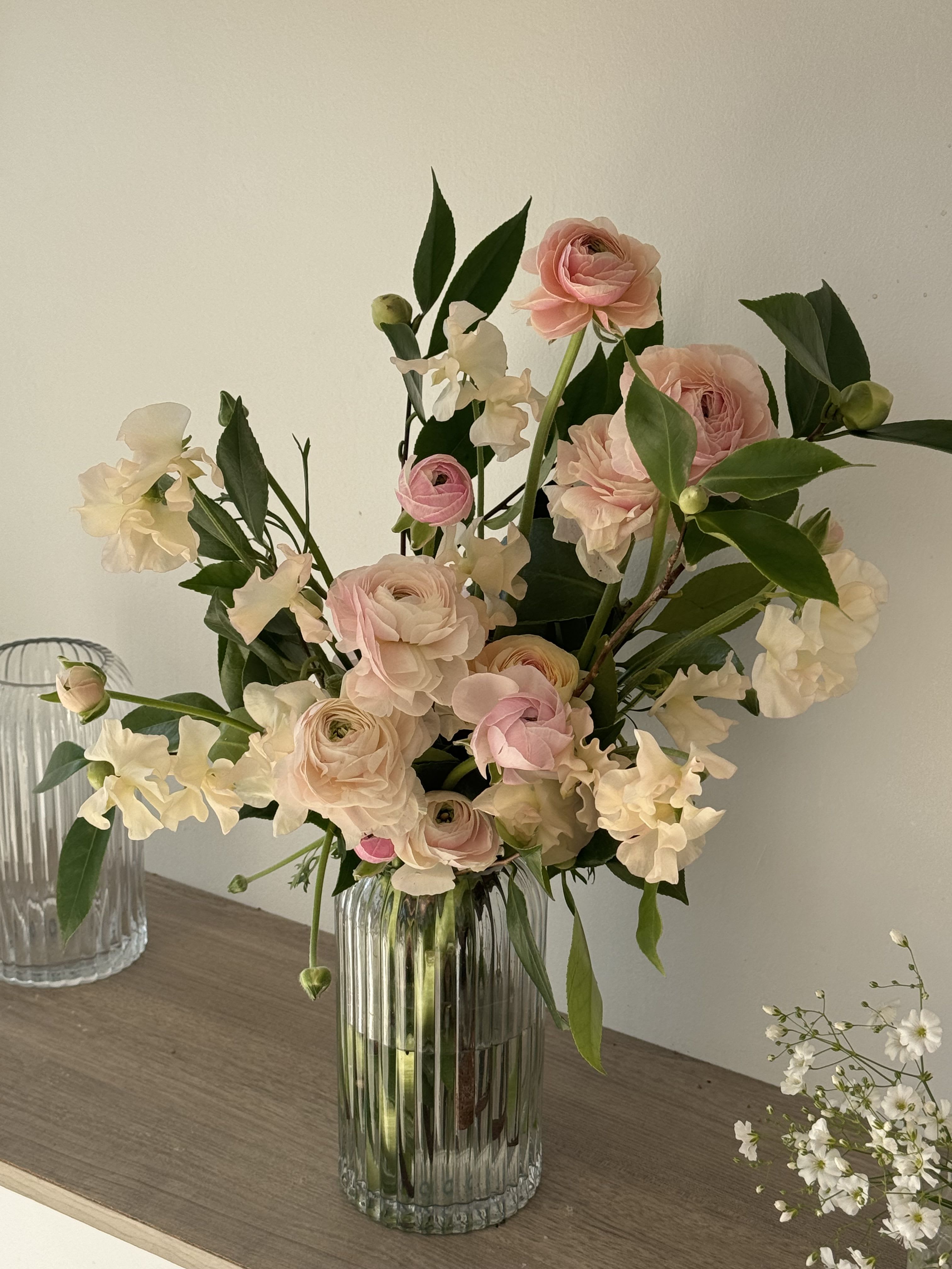 Blush pink ranunculus and white sweet pea in a clear glass vase