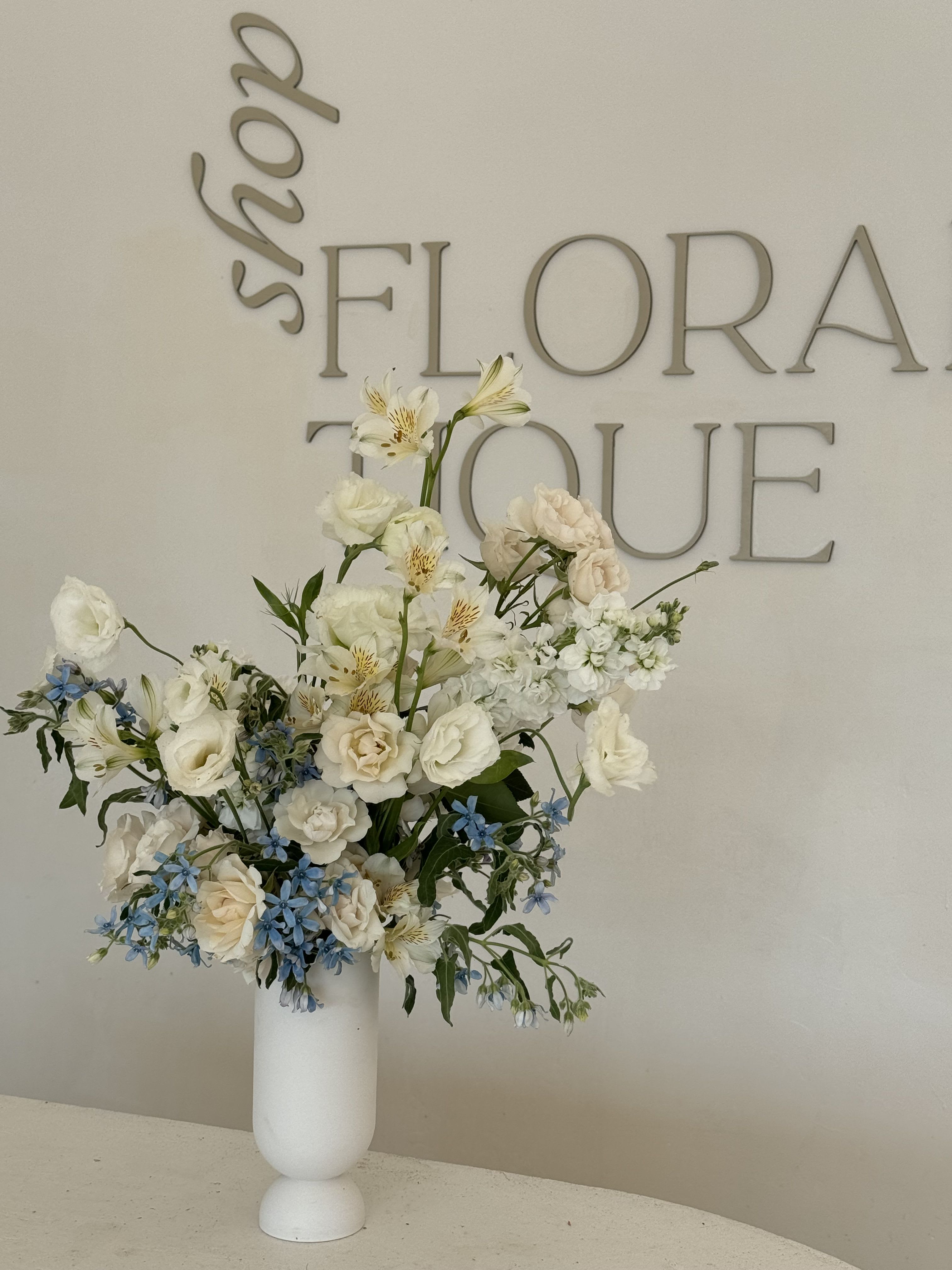 Tall white floral arrangement in a white vase with blue accents