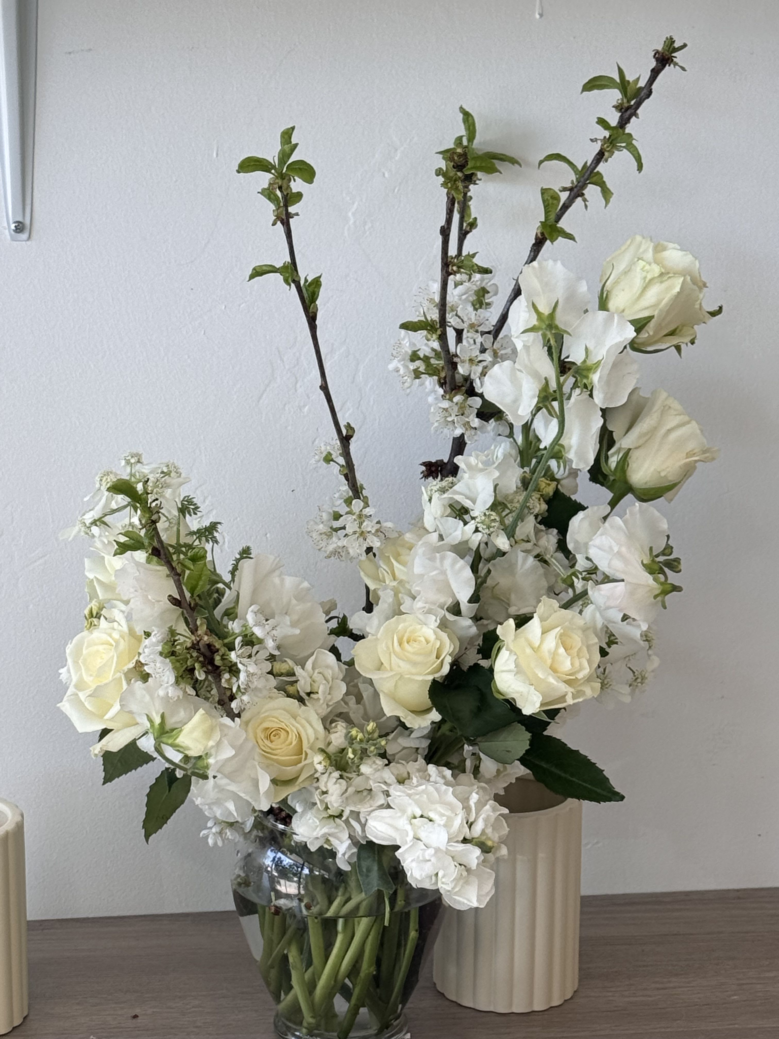 White roses and blossoms arranged in a clear glass vase