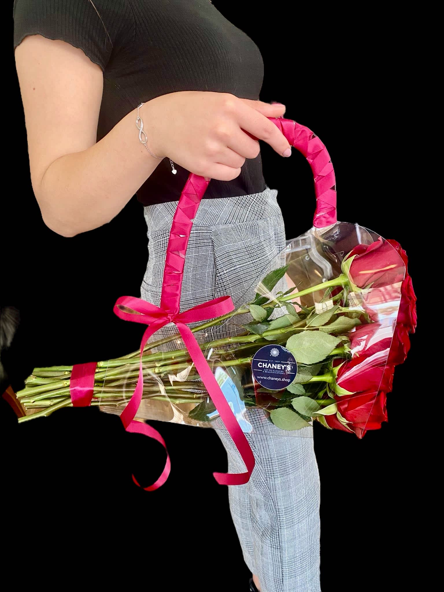 A hand holds a bouquet of red roses wrapped in clear plastic with a pink ribbon.