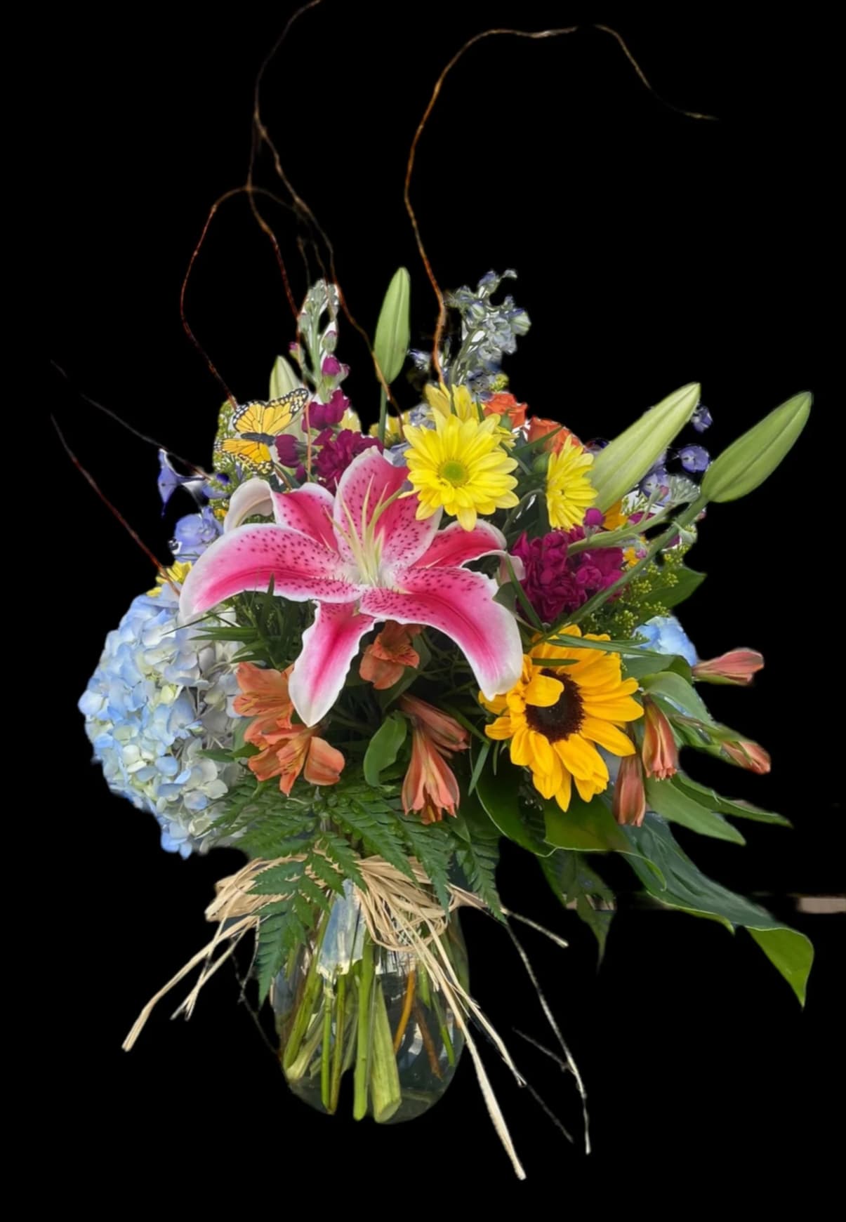 Mixed bouquet with pink lily, sunflowers, and blue hydrangea in a glass vase