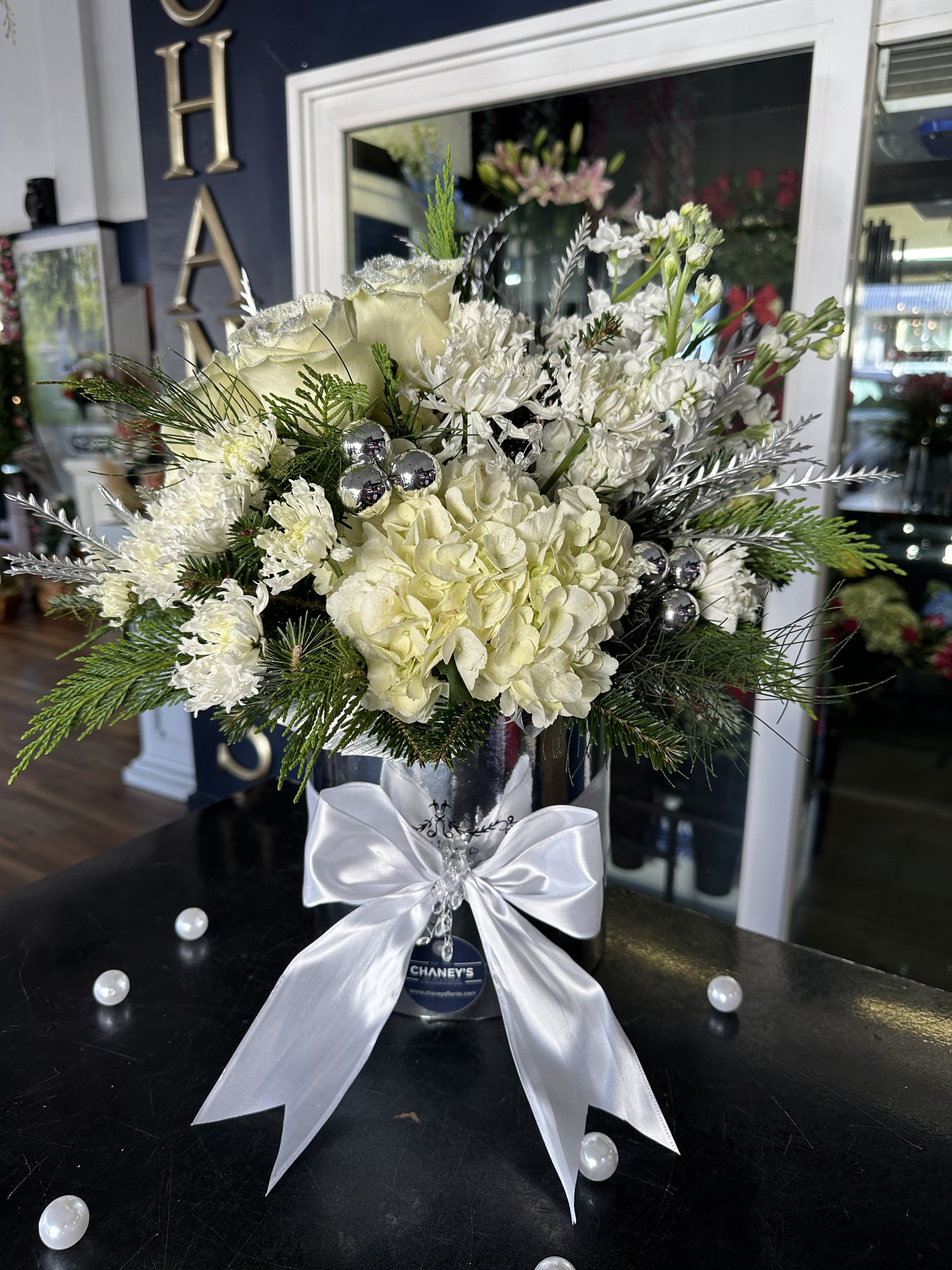 White floral arrangement in a silver vase with a satin bow