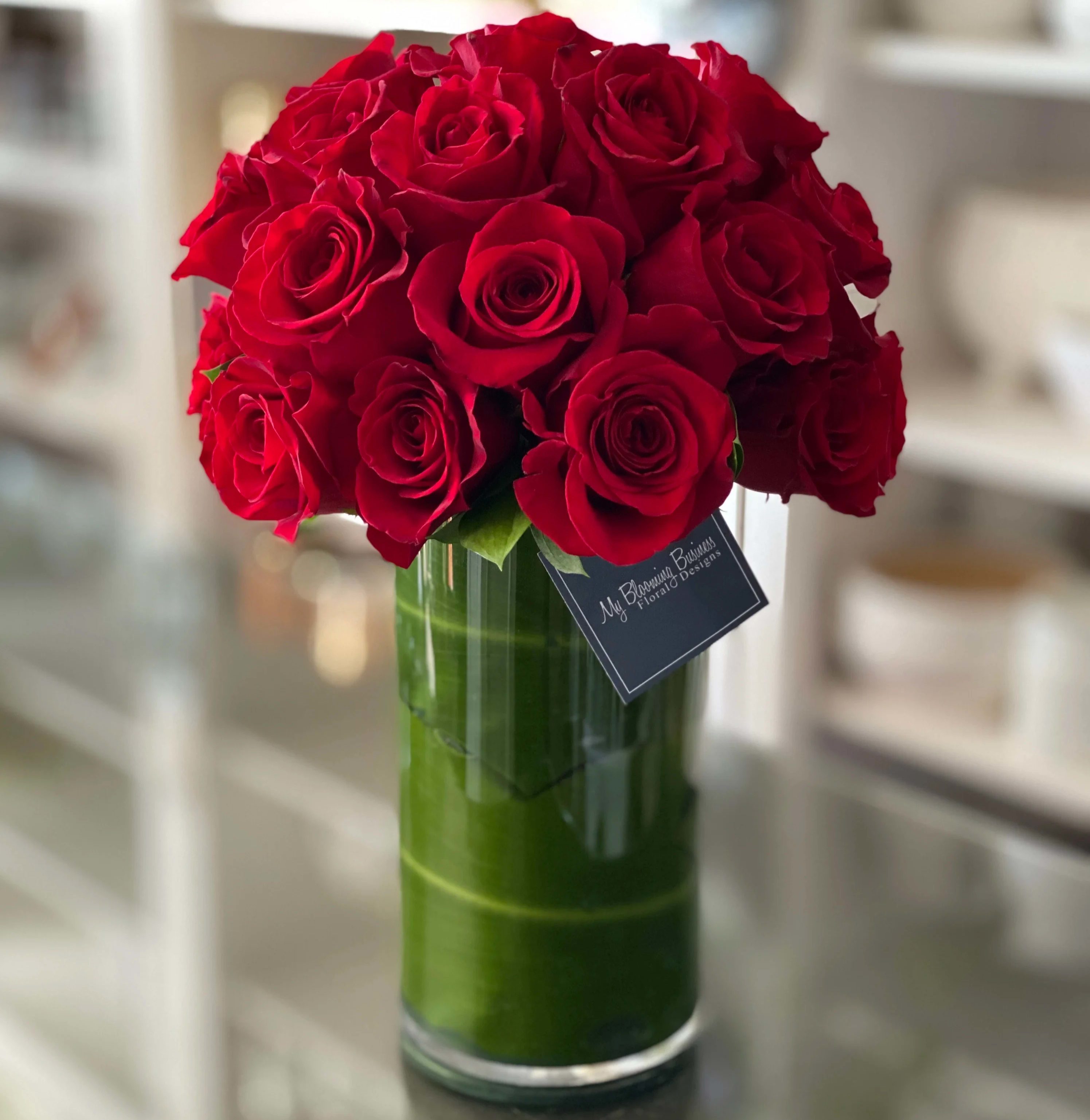Madly In Love - FB - Introducing Madly in Love, the ultimate gift that will make your loved ones weak at the knees! Get ready to woo their hearts and sweep them off their feet with a spectacular display of romance, elegance, and passion. We've combined two dozen mesmerizing red roses with a 10" clear cylinder vase lined with T leaf, creating a stunning masterpiece that will leave your family and friends utterly enchanted. 