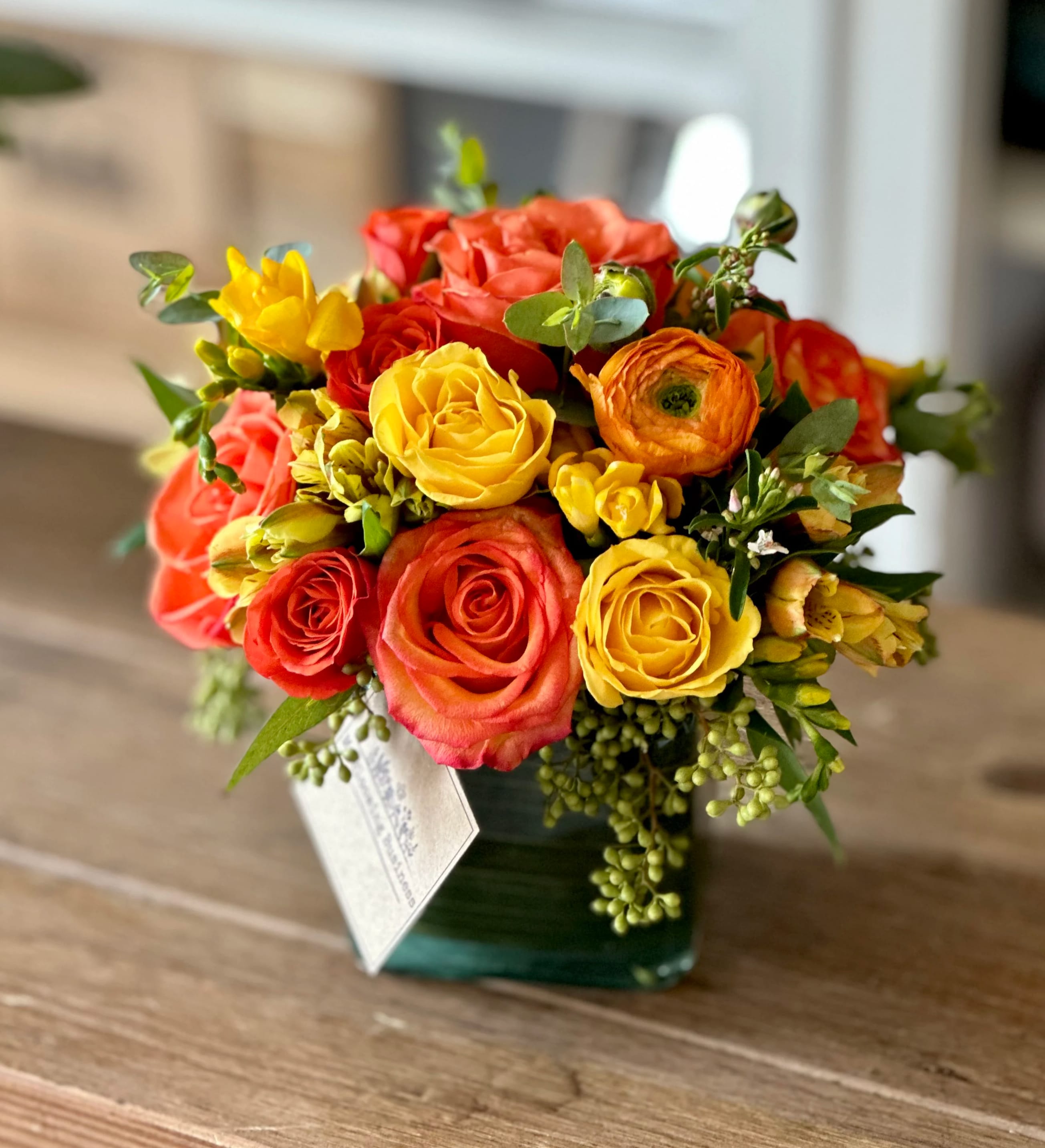 Bouquet of yellow, orange, and coral roses in a square glass vase