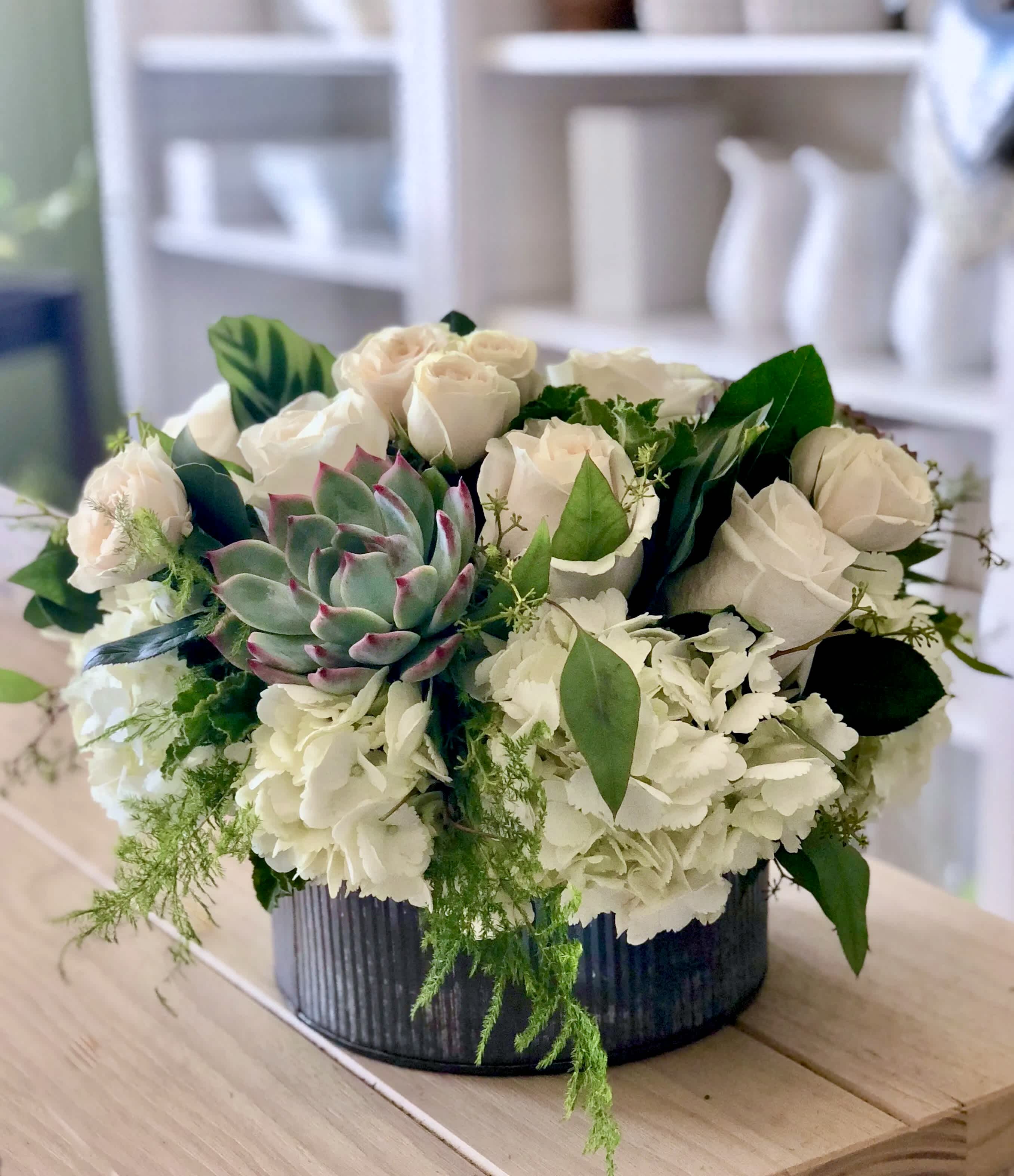 White roses and hydrangeas with a succulent in a dark round container