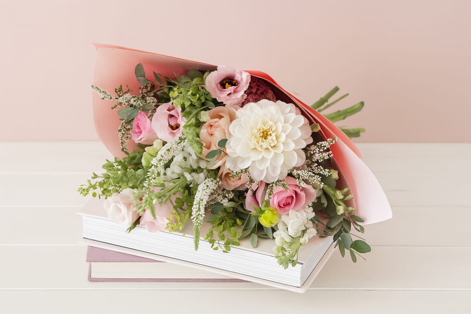 Pink and white bouquet wrapped in coral paper, resting on books