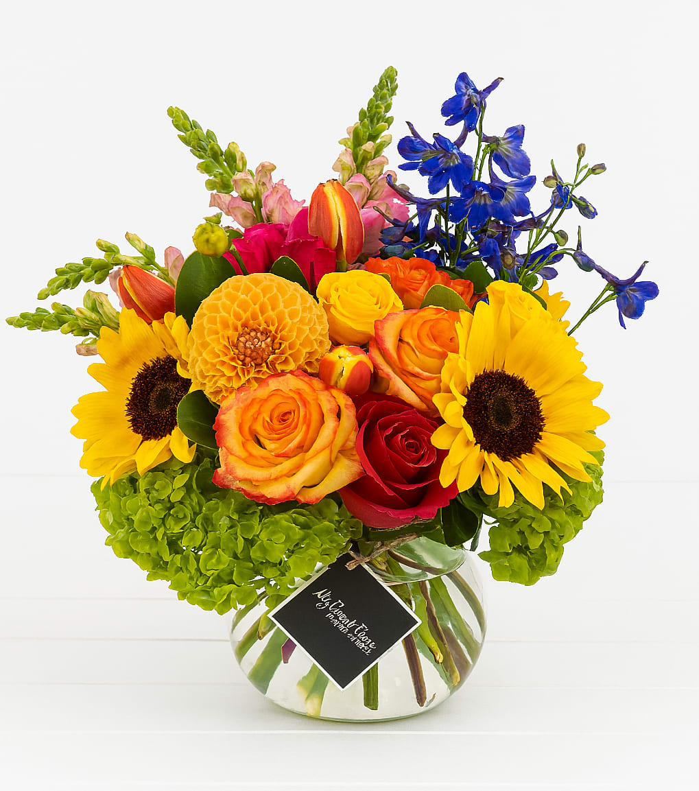 Bright mixed bouquet in a round glass vase with sunflowers and roses