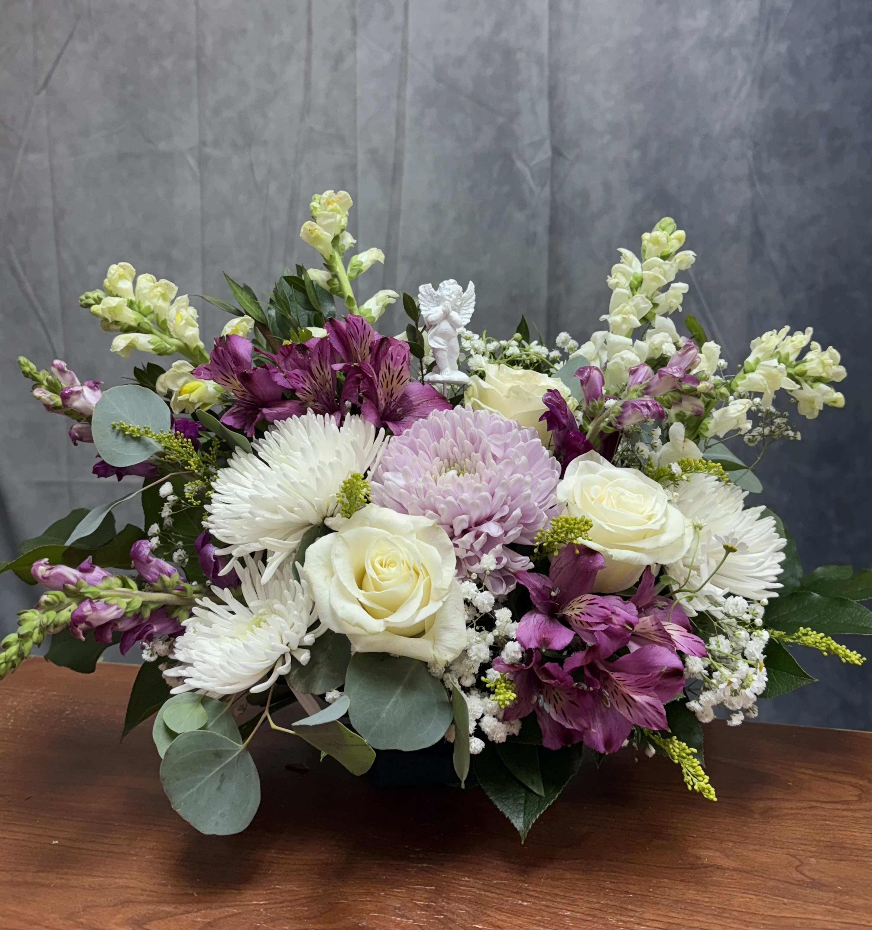 Mixed bouquet of white roses, purple flowers, and white daisies in a low container