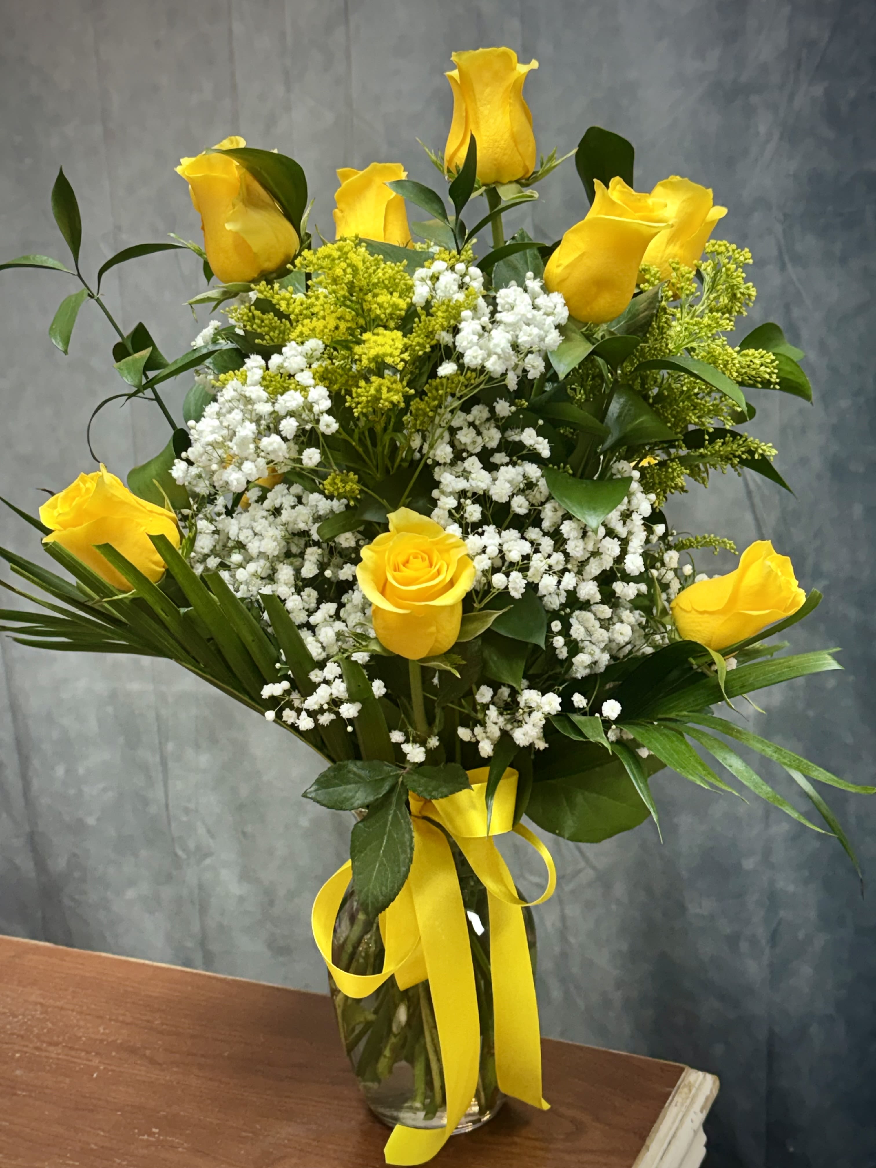 Yellow roses and white baby's breath in a glass vase with a yellow ribbon