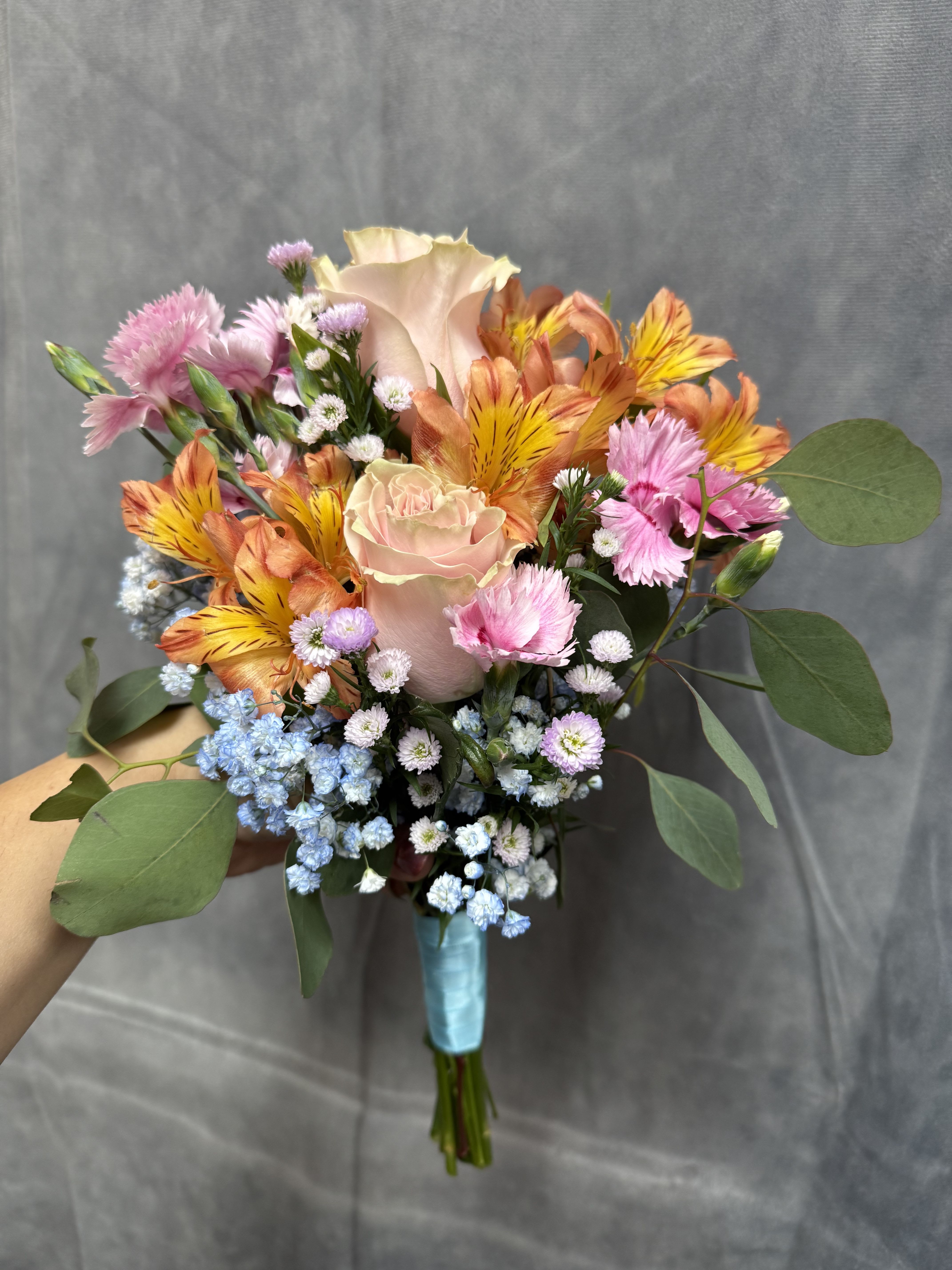 Spring Sorbet Prom bouquet  - Soft pink roses, bright orange alstroemeria, pink mini carnations and blue baby breath with greenery, hand-tied with ribbon for a cheerful,  spring bouquet perfect for prom 