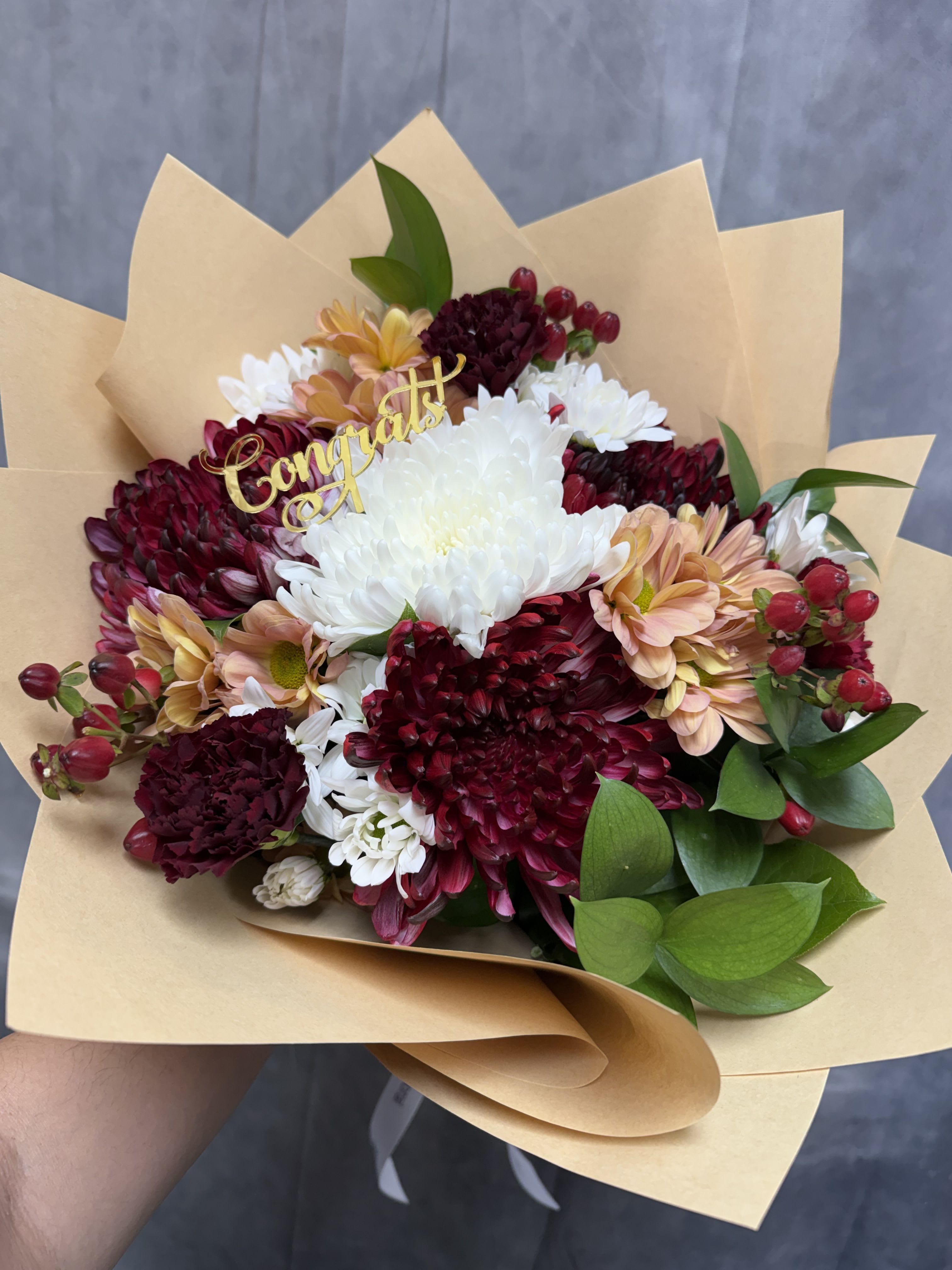 Burgundy Charm Bouquet  - A rich and cheerful mix of burgundy chrysanthemums, white mums, peach daisies, and vibrant berries, finished with a festive “Congrats” topper. Perfect for graduations, promotions, and special achievements.