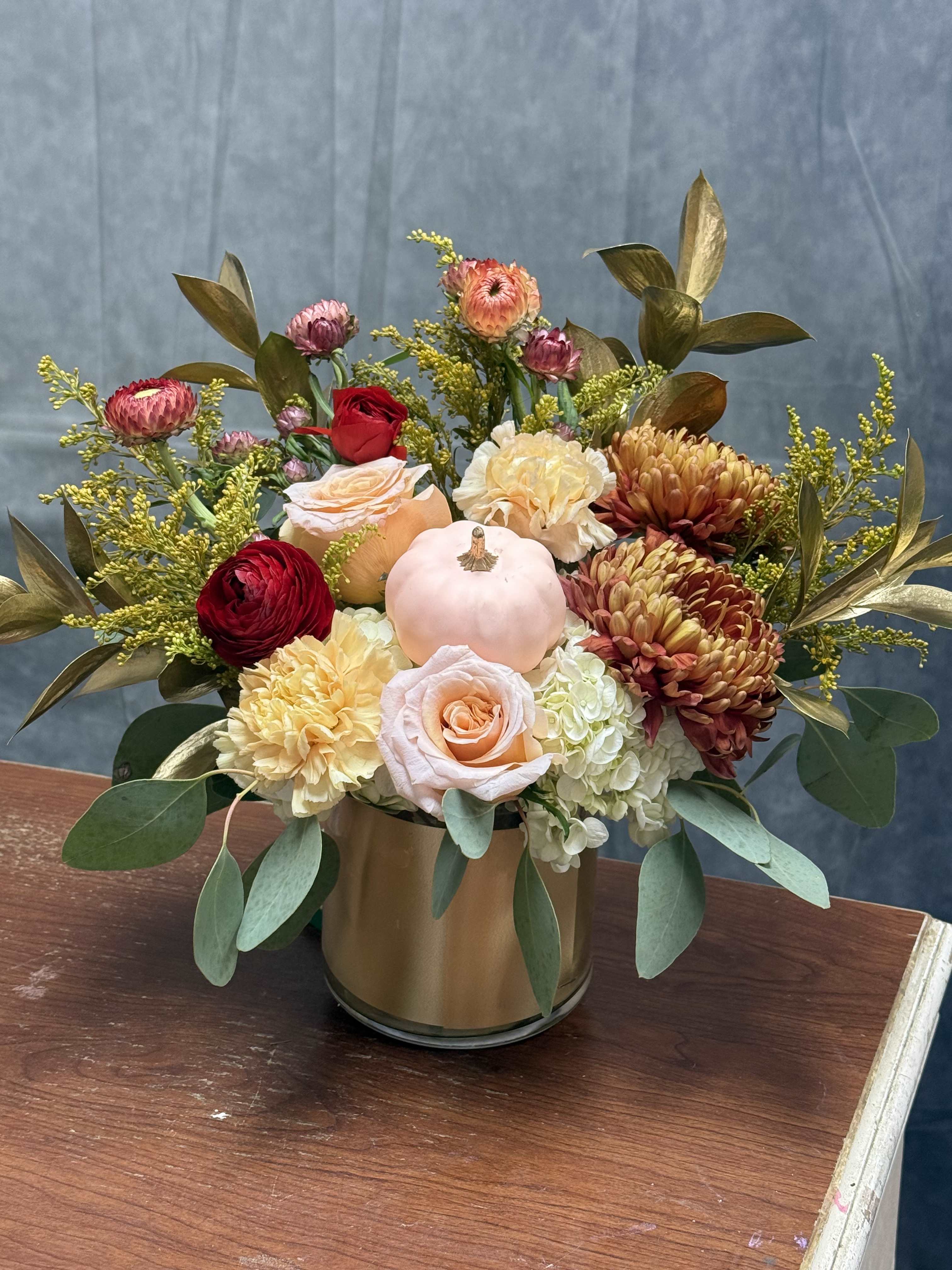 Mixed bouquet in a gold vase with roses, chrysanthemums, and a small pumpkin