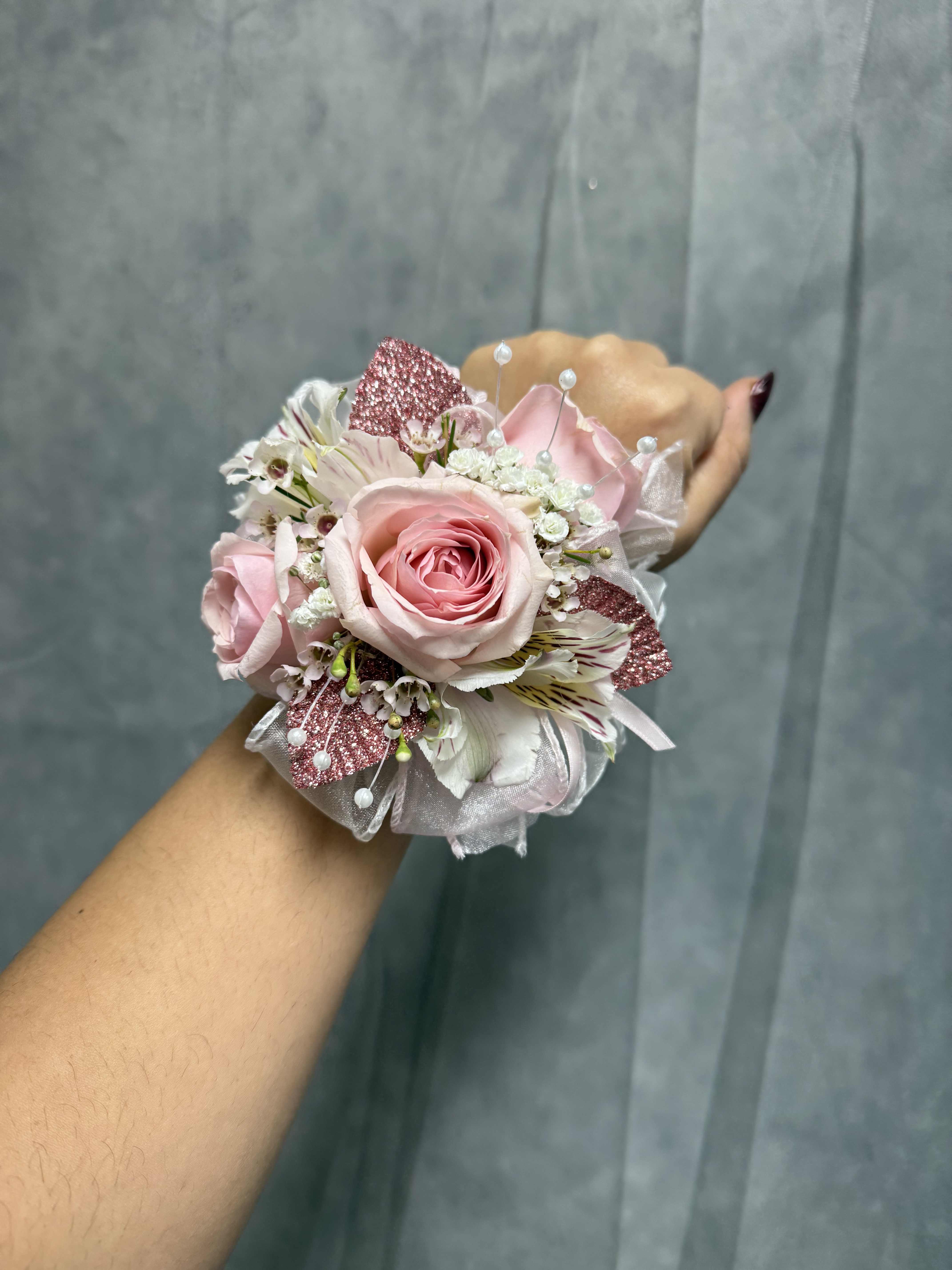 Small pink rose corsage with white accents worn on a wrist