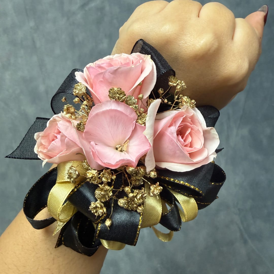 Pink rose wrist corsage with black and gold ribbon on a person's wrist