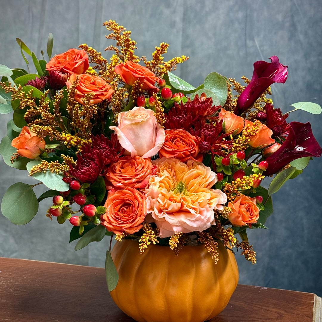 Orange and burgundy floral arrangement in a pumpkin-shaped vase