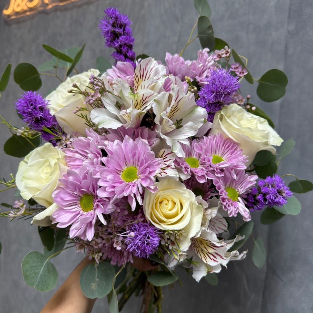 Handheld bouquet of pink daisies, white roses, and purple flowers