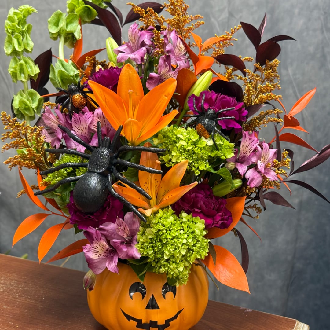 Halloween bouquet in a jack-o'-lantern container with orange lilies and purple flowers