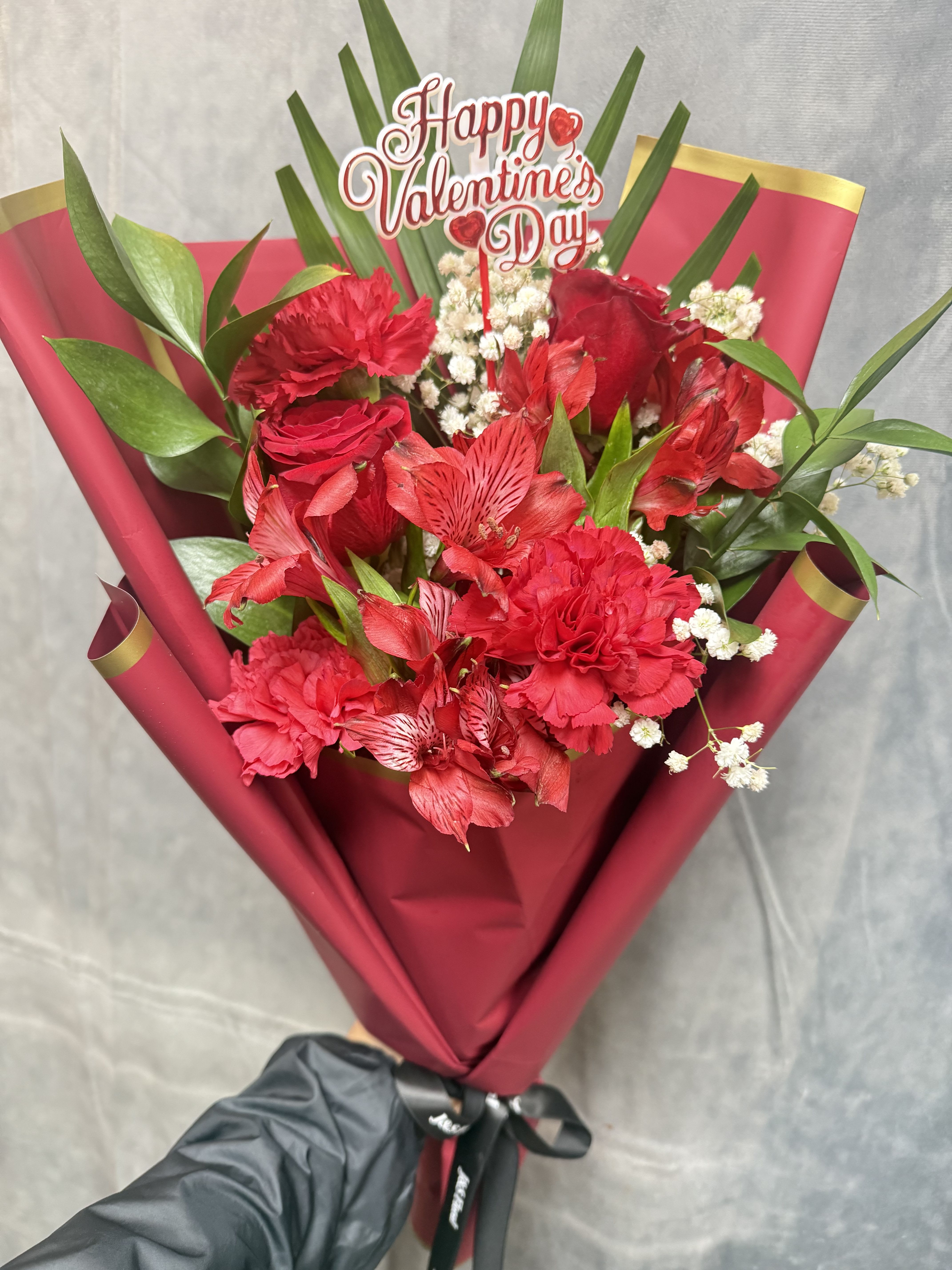Mix Red Layered Bouquet  - A romantic hand-tied bouquet featuring rich red roses, carnations, and alstroemeria, delicately accented with baby’s breath and lush greenery. Wrapped in elegant deep-red paper for a bold, timeless statement of love and passion. ️