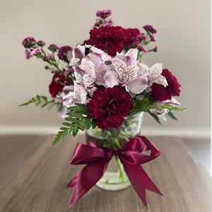 Bouquet of burgundy and pale pink flowers in a glass vase with a ribbon