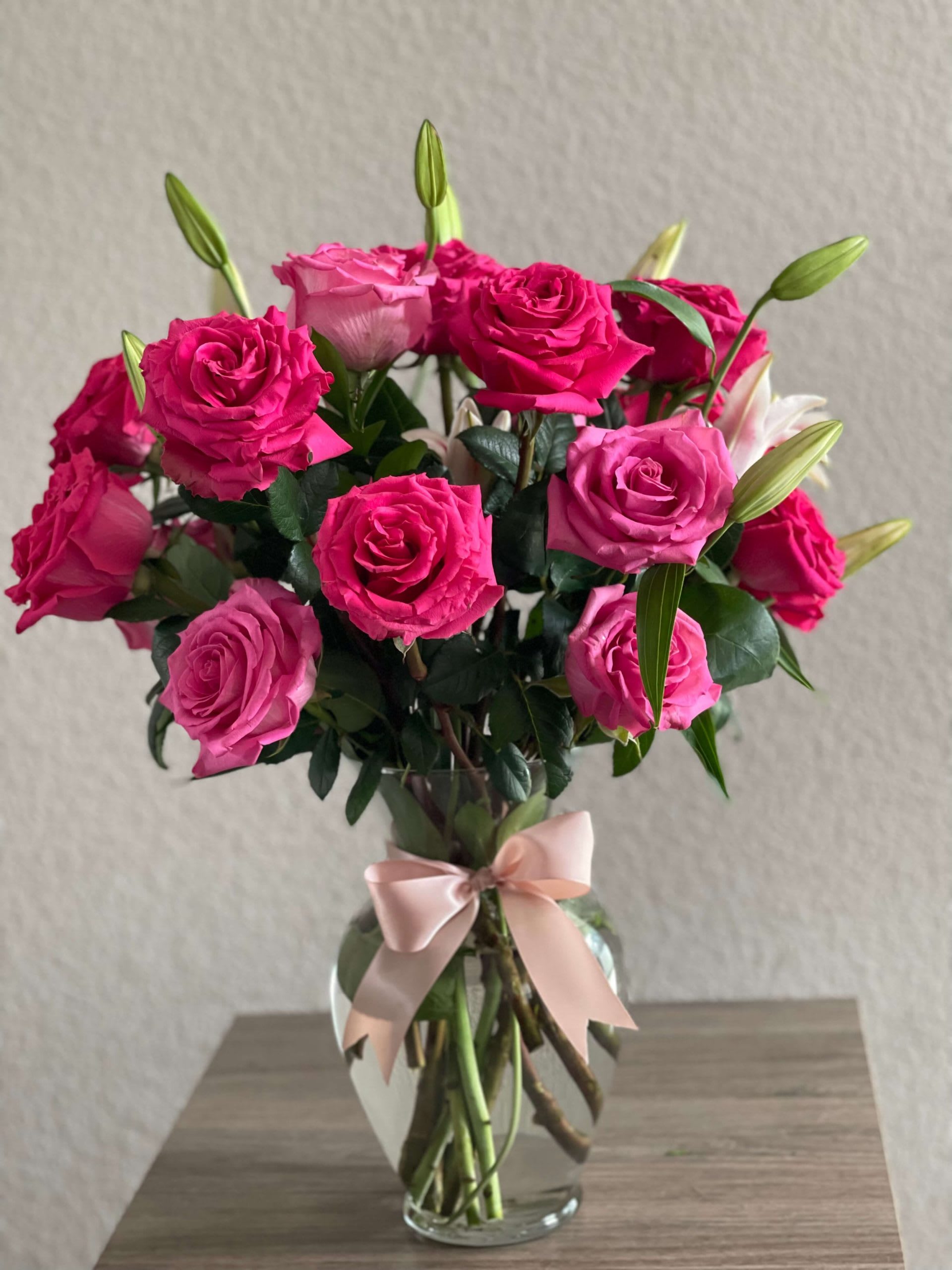Pink roses and lily buds arranged in a glass vase with a ribbon