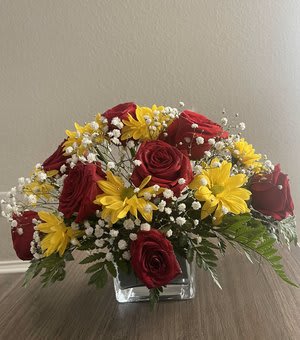 Red roses and yellow daisies in a clear square vase