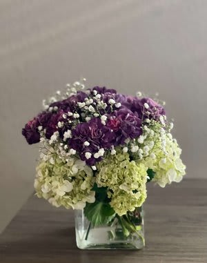 Purple and green hydrangea bouquet in a clear square vase