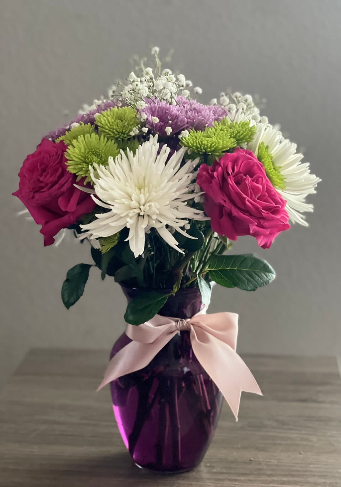 Pink roses and white chrysanthemums in a purple vase with a ribbon