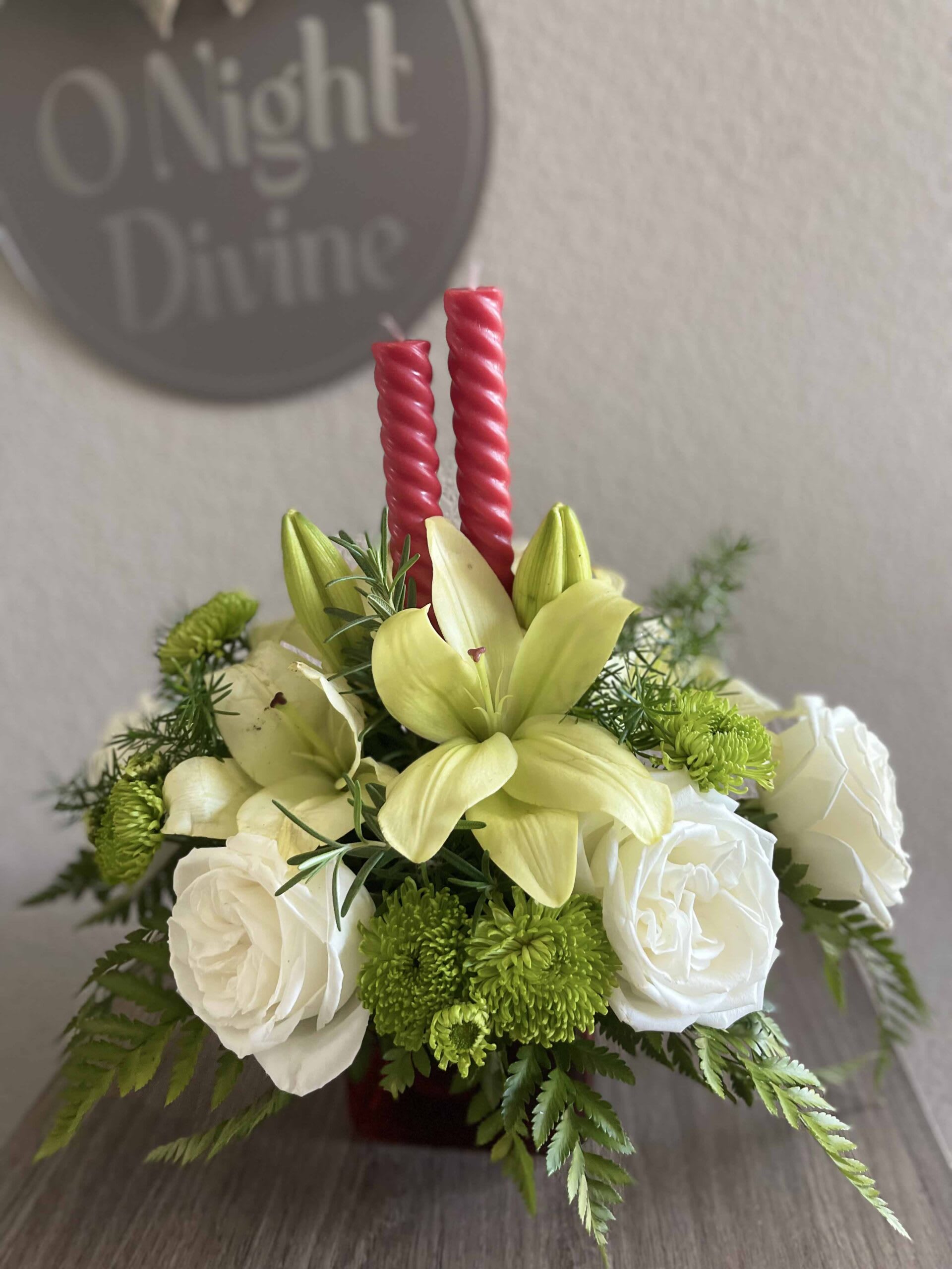White roses and pale yellow lilies arranged with red candles.