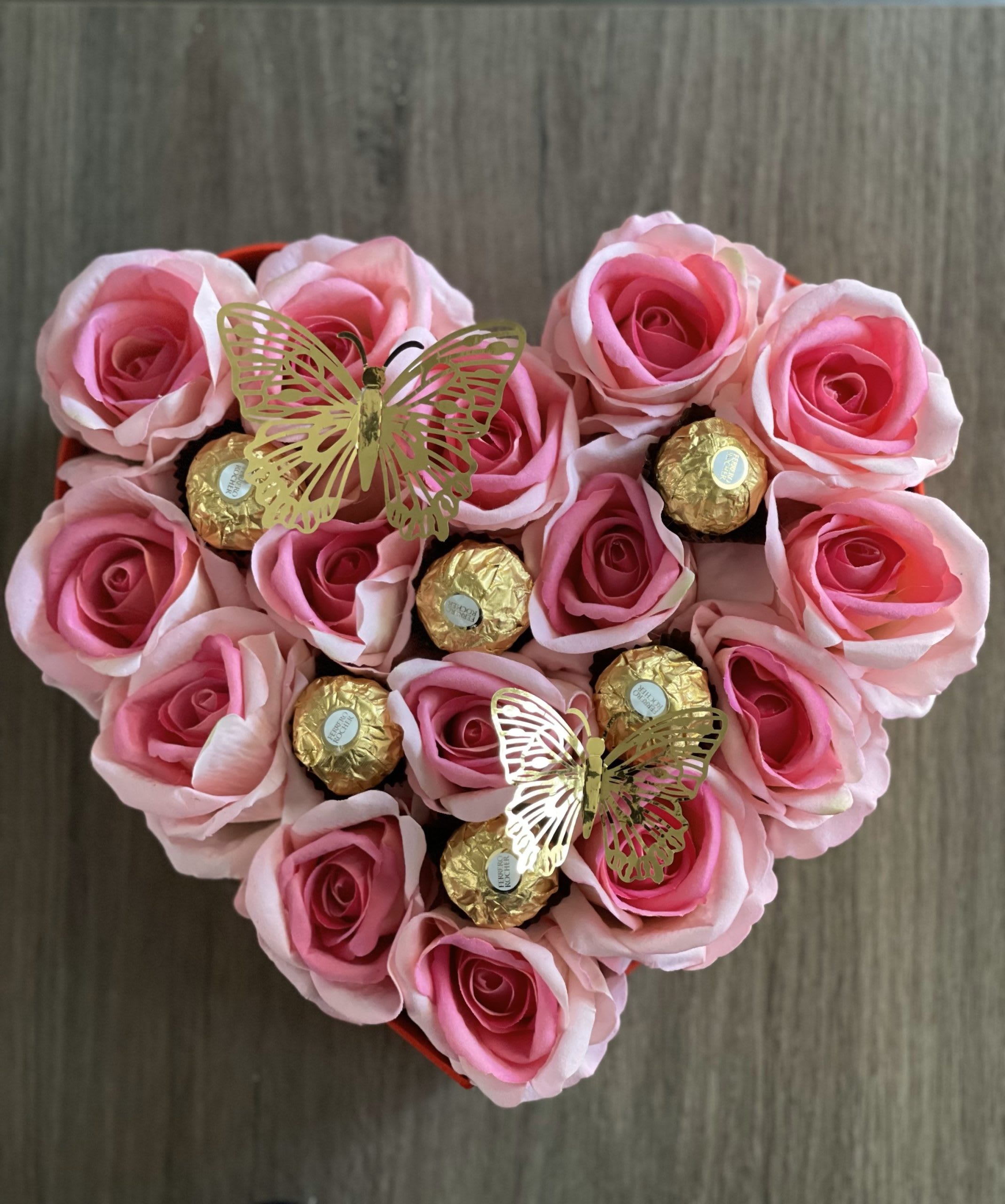 Heart-shaped box of pink roses with gold-wrapped chocolates and butterfly picks