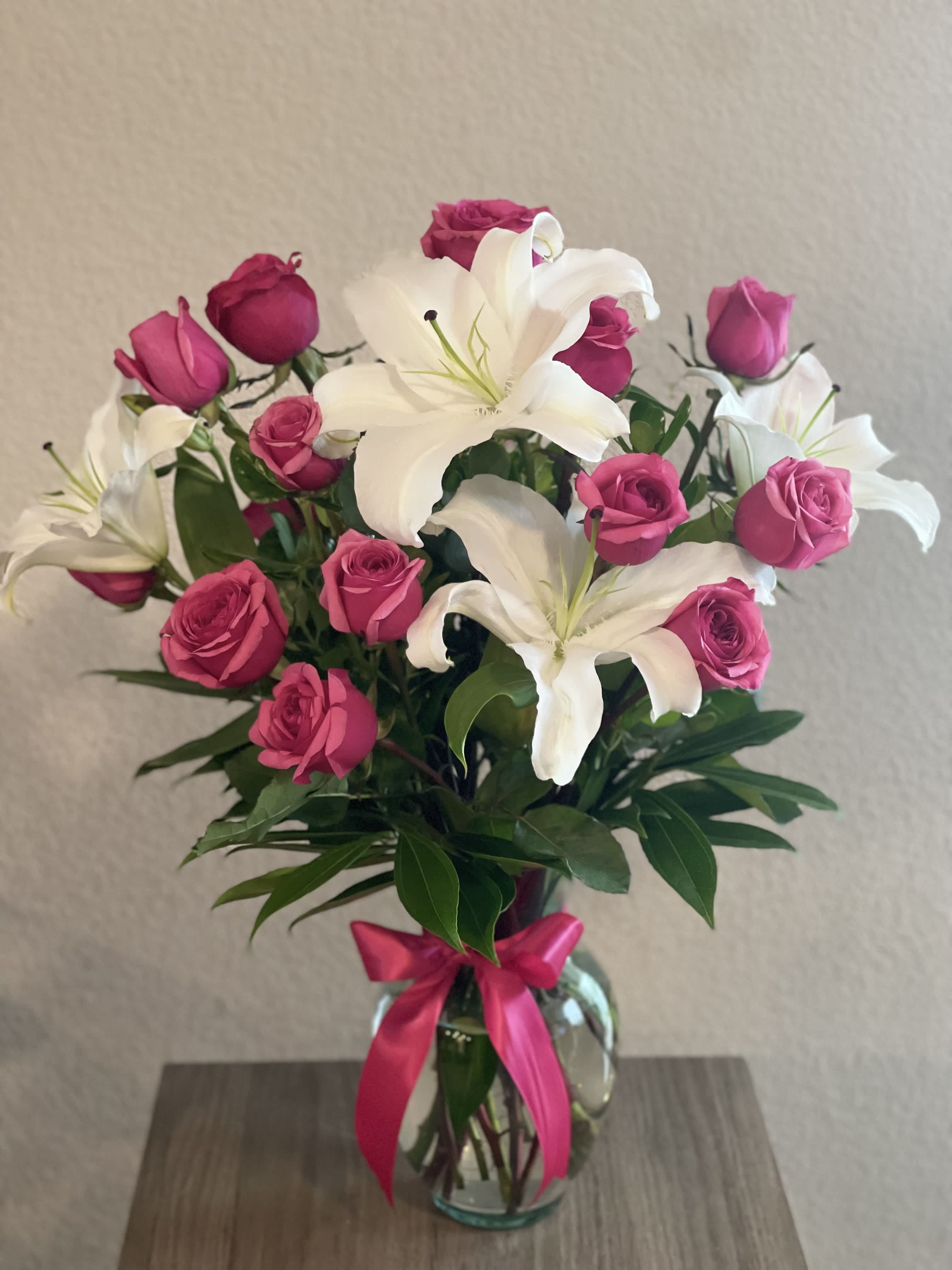 Pink roses and white lilies in a glass vase with a pink ribbon