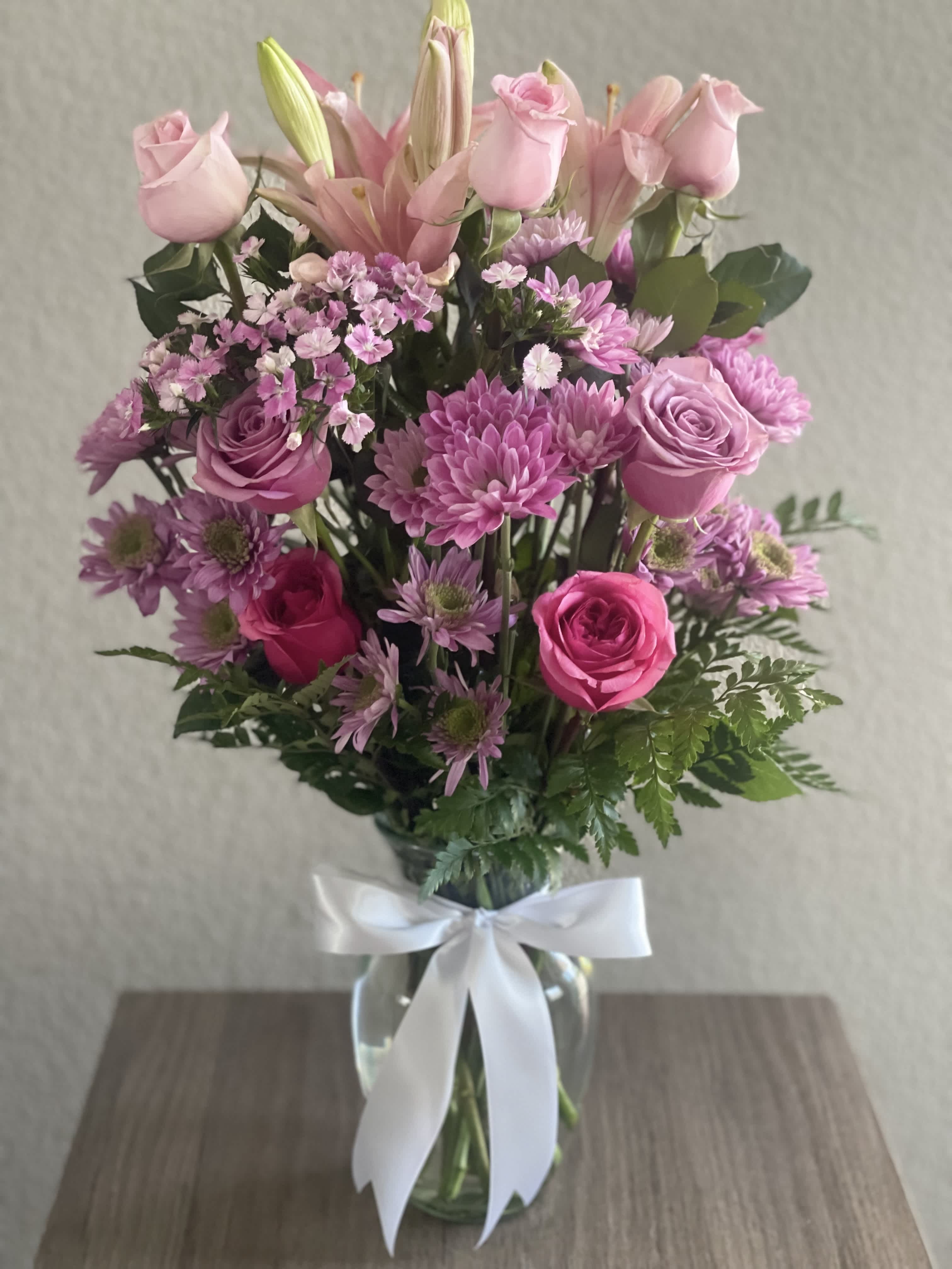Pink roses and lilies arranged in a glass vase with a white ribbon