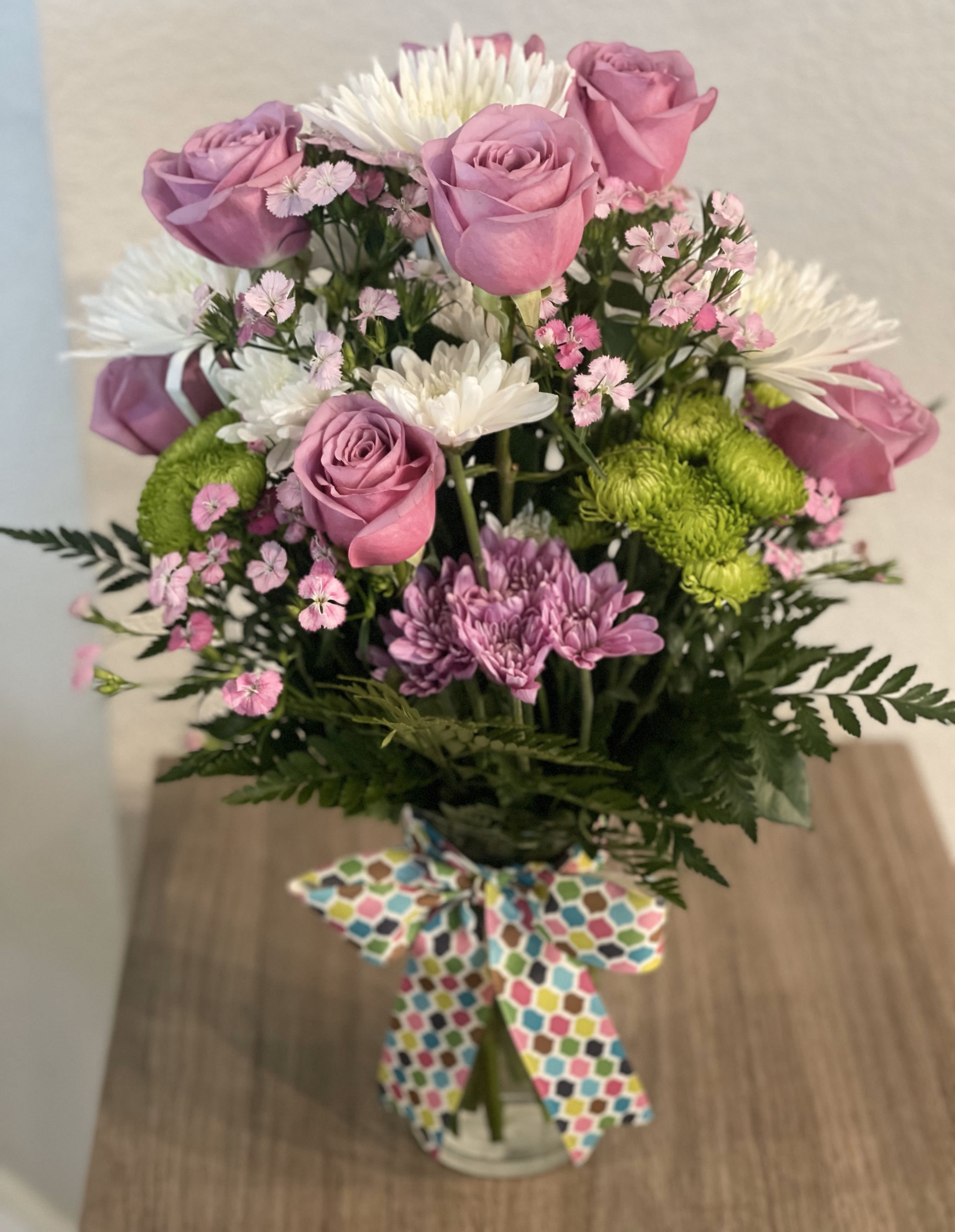 Bouquet of pink roses, white daisies, and green mums in a glass vase