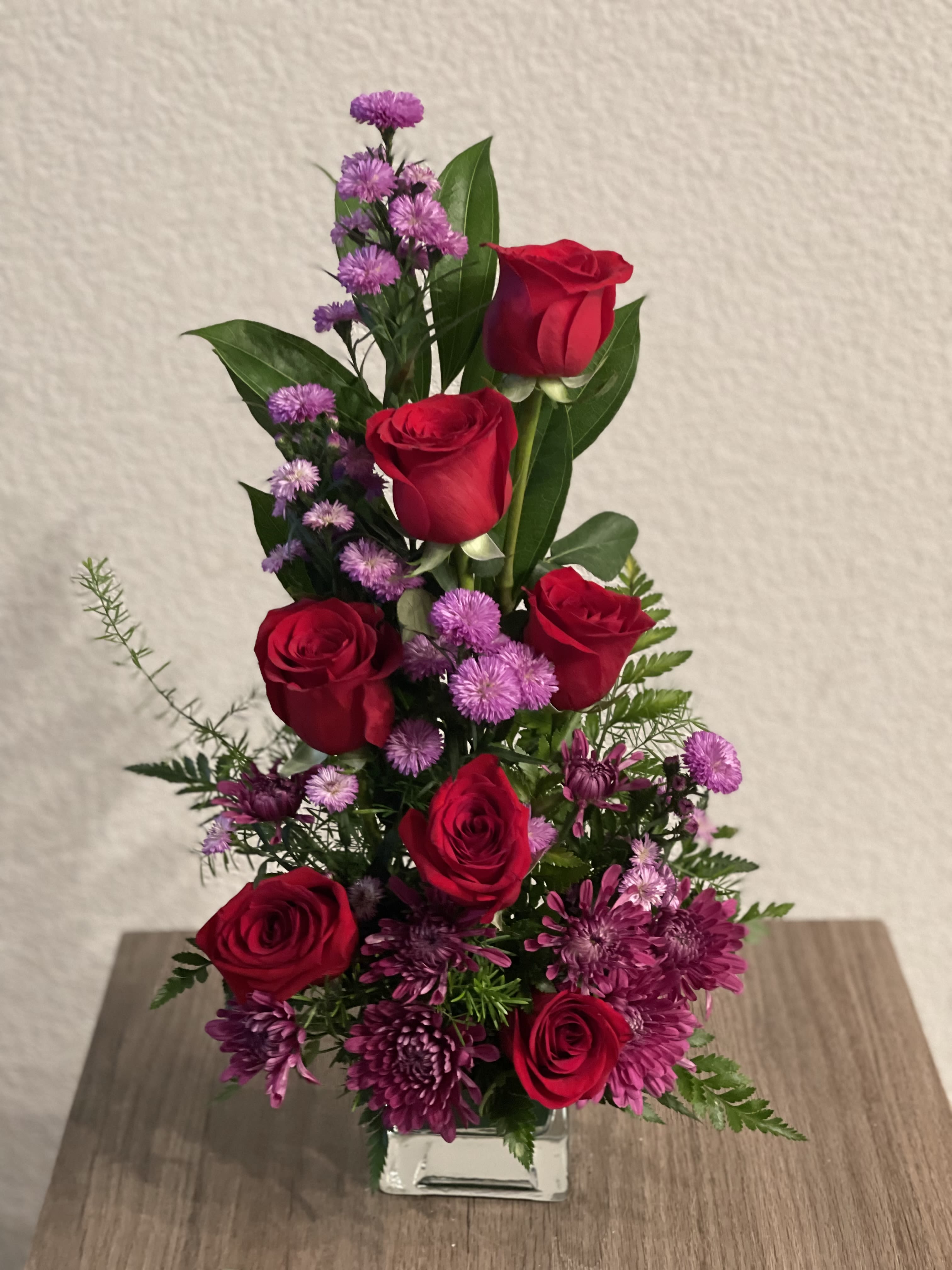 Red roses and purple flowers in a clear glass vase