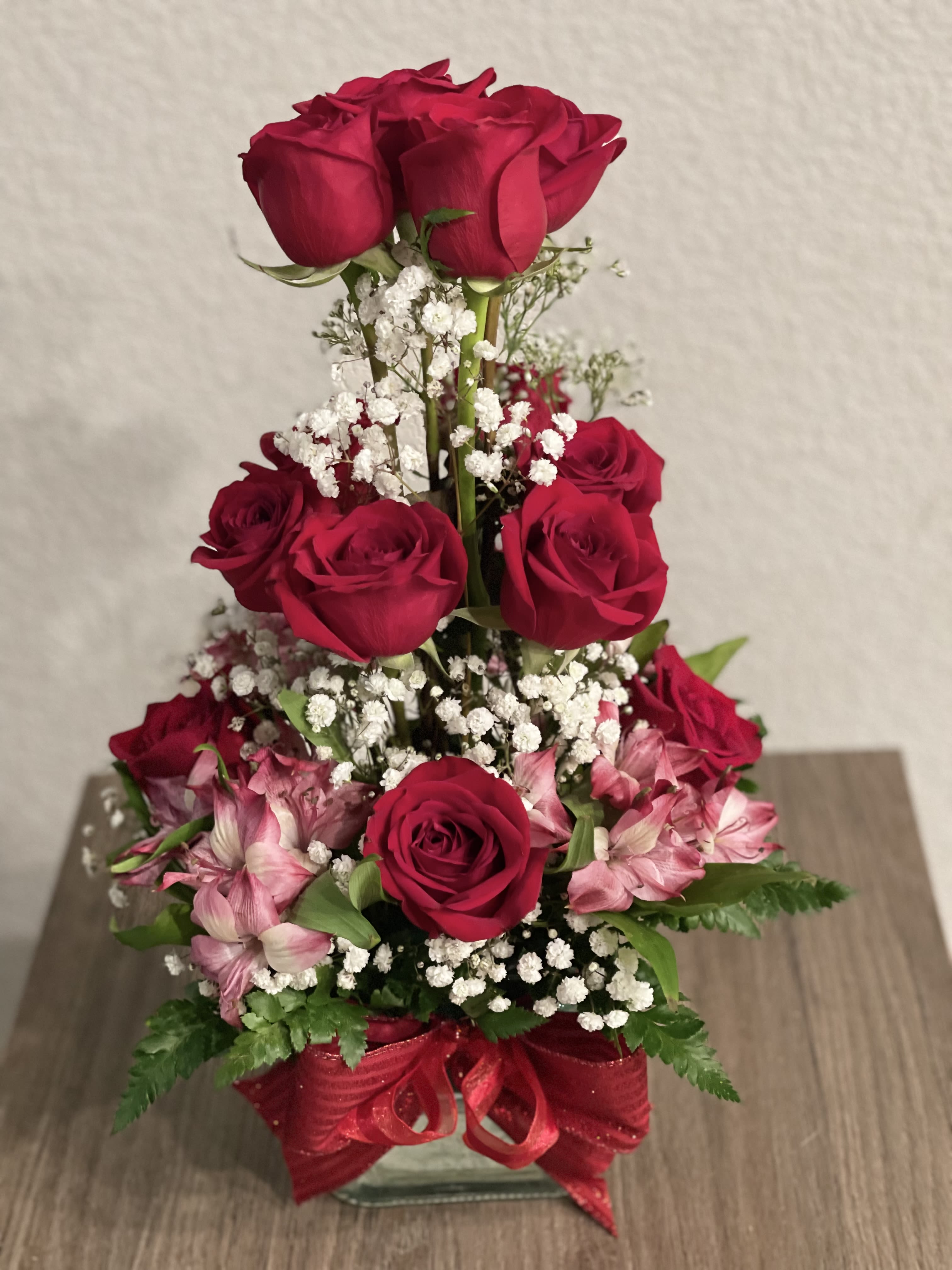 Tiered bouquet of red roses and pink flowers in a glass vase with a red ribbon