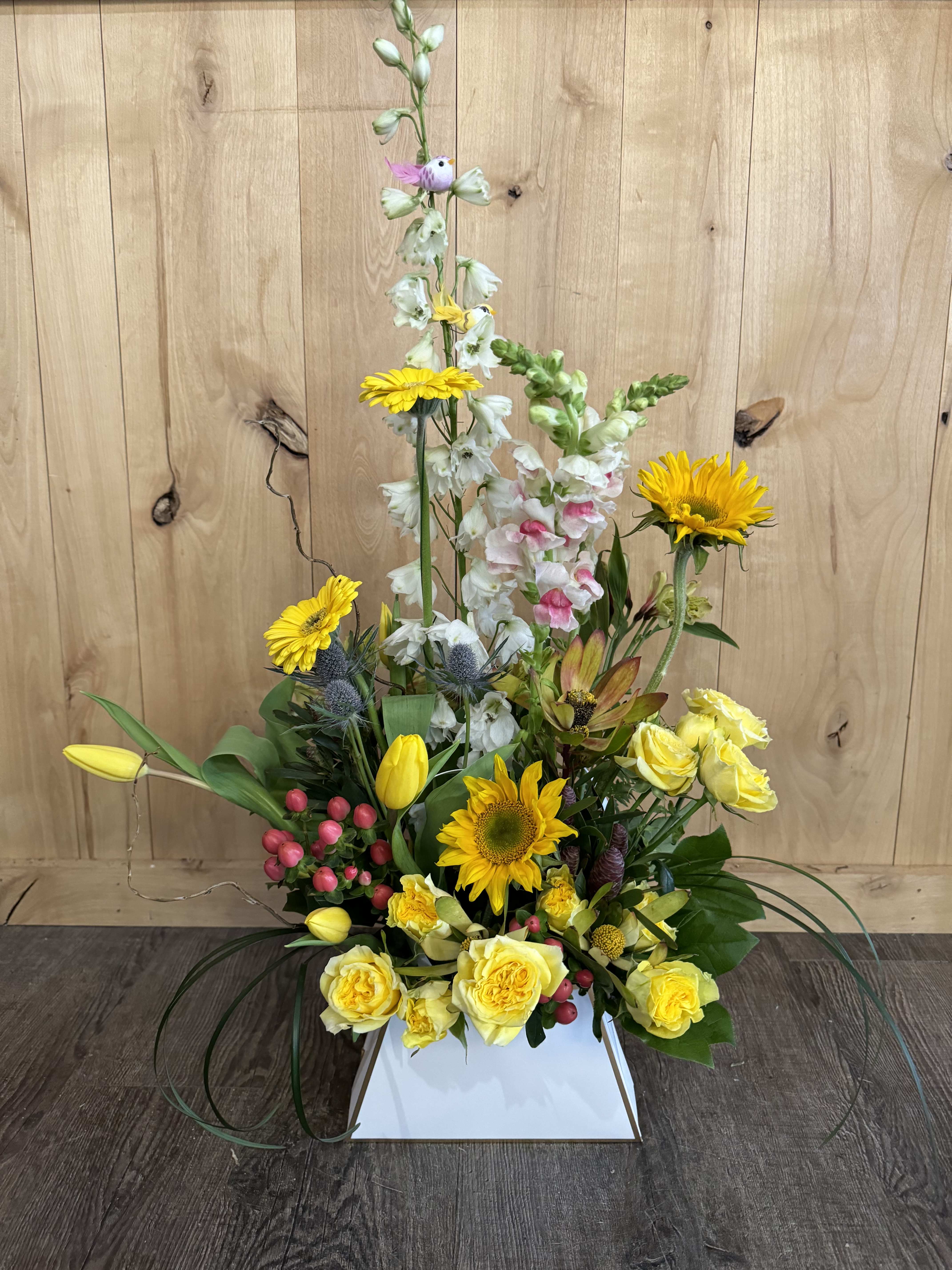 Tall floral arrangement with yellow roses, sunflowers, and white snapdragons in a white box