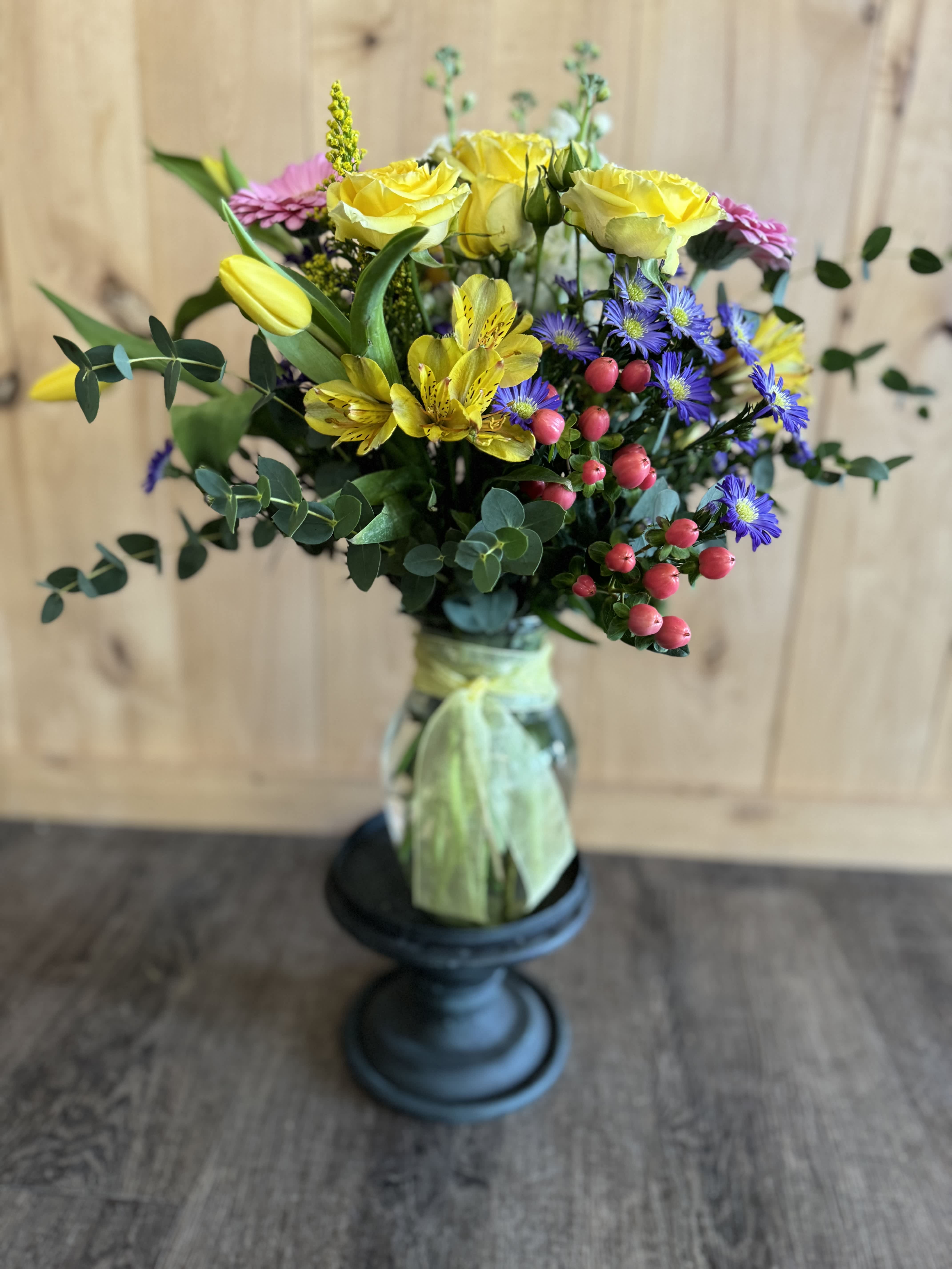Bouquet of yellow roses, purple daisies, and pink blooms in a glass vase