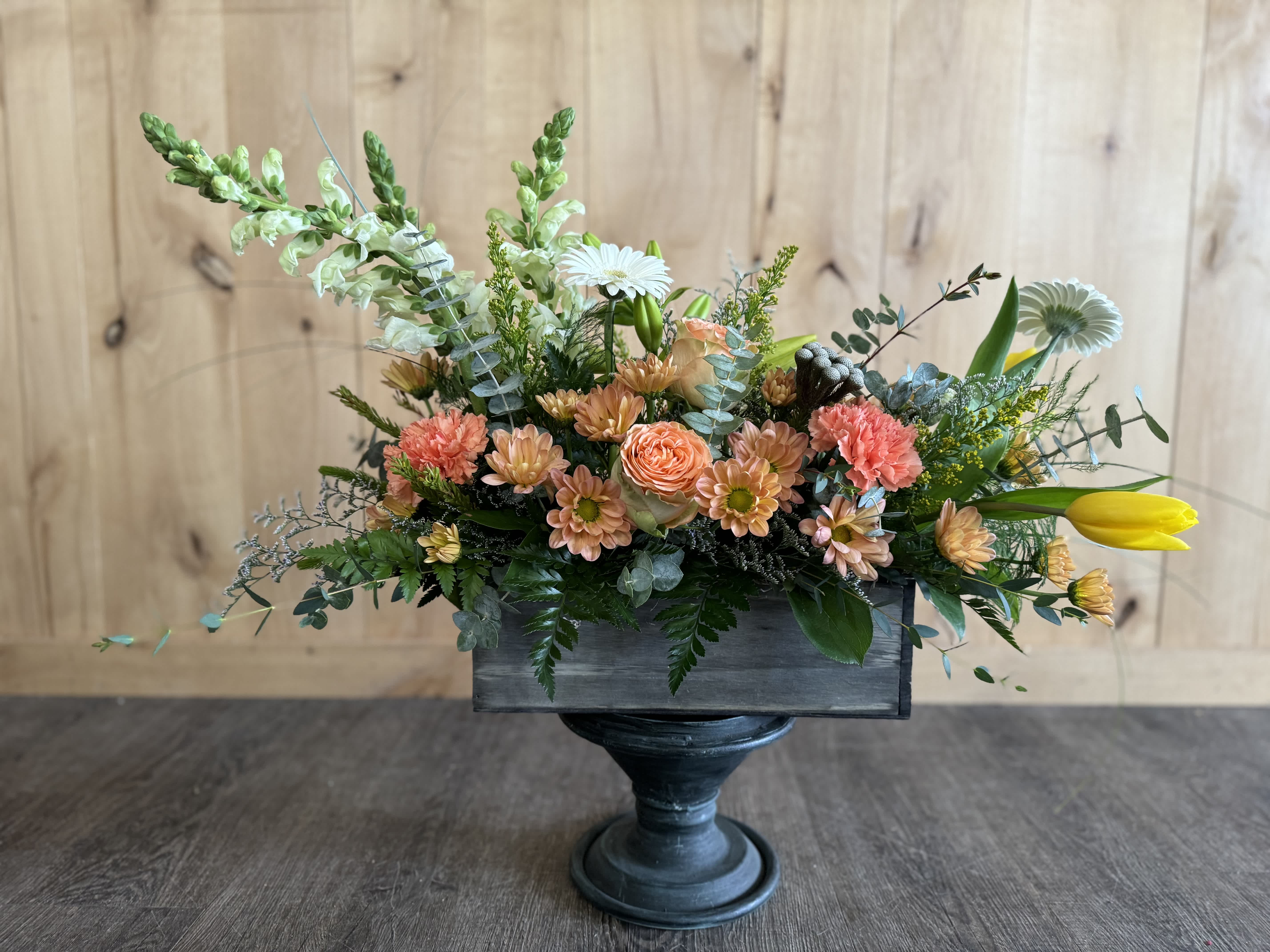 Mixed floral arrangement in a dark wooden container on a pedestal stand