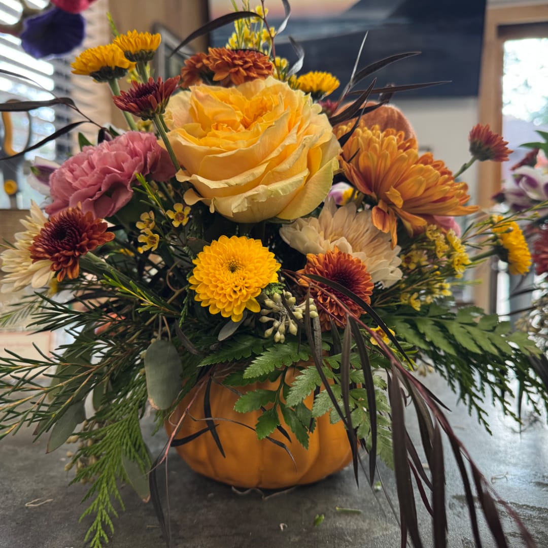 Mixed autumn bouquet in a pumpkin container with a yellow rose and chrysanthemums