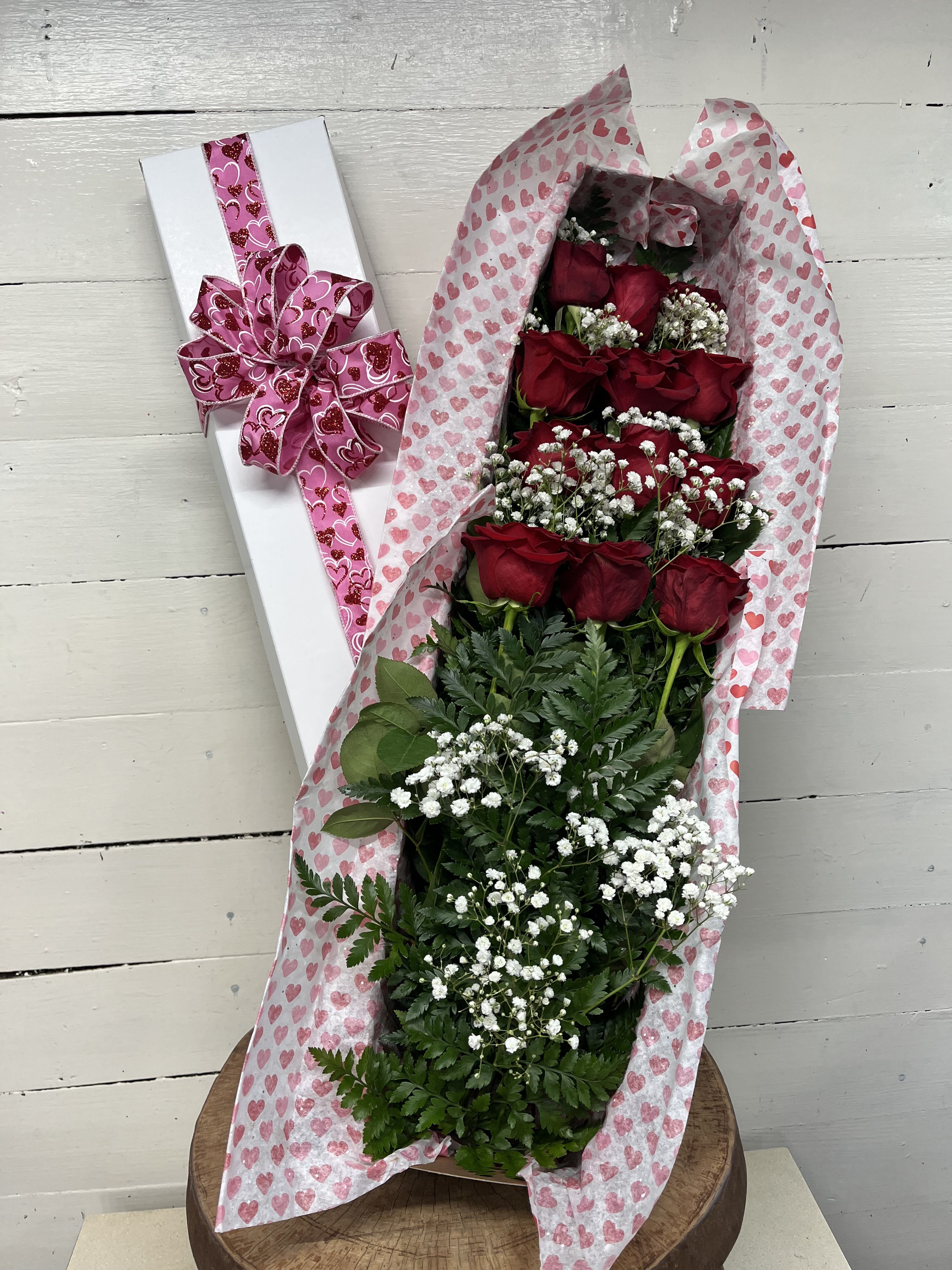 Bouquet of red roses in heart-patterned wrap beside a white gift box with pink ribbon