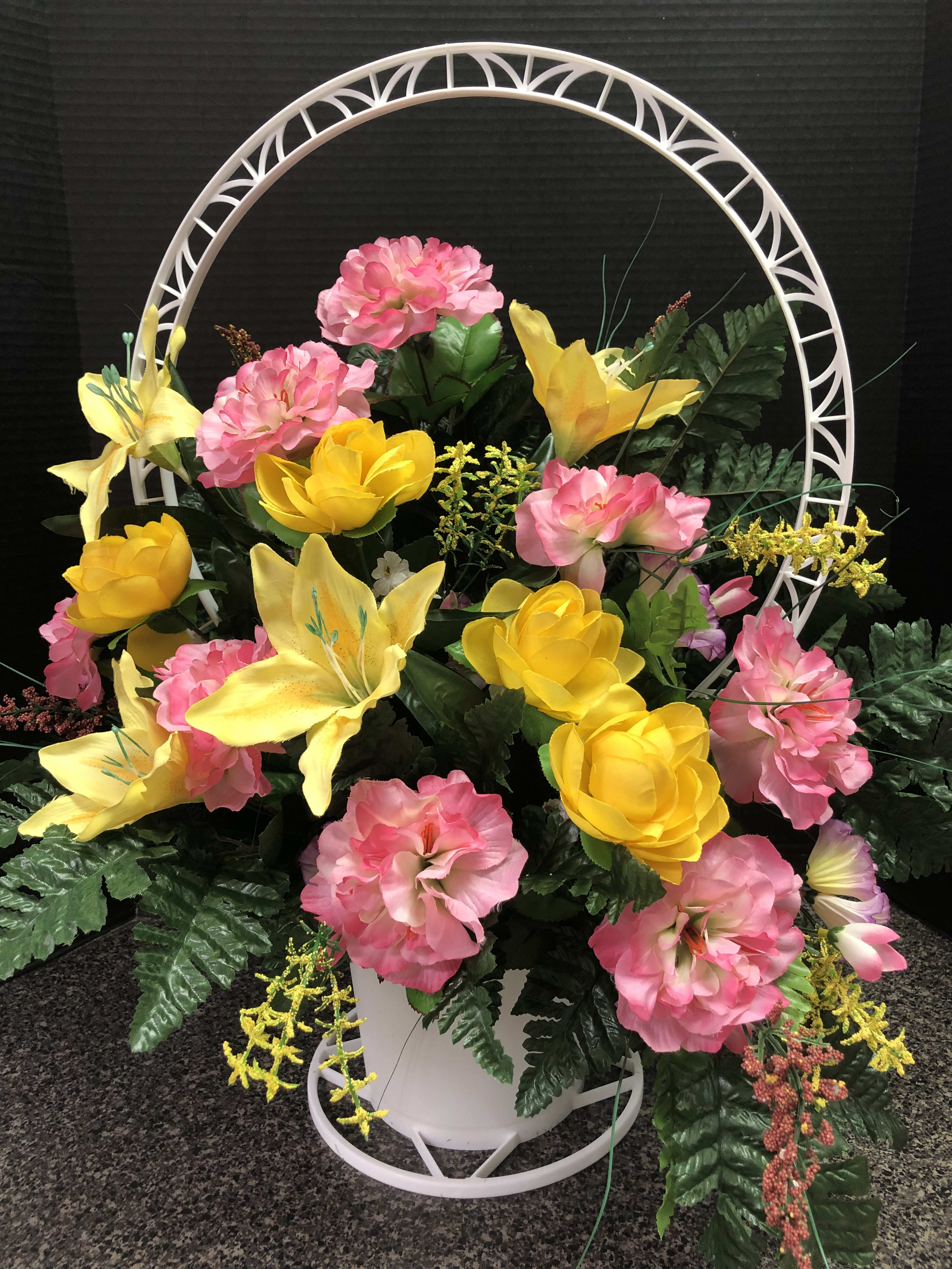 Pink and yellow floral arrangement in a white basket with a circular frame